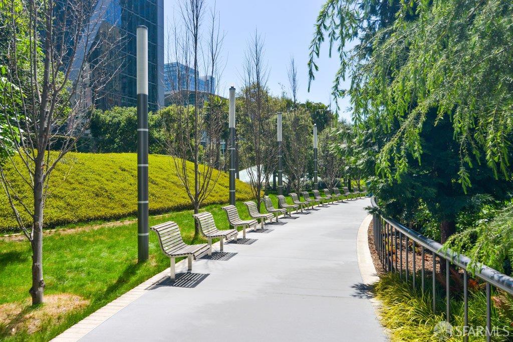 Landscaped walkway curves past a row of benches and trees beside a modern building.
