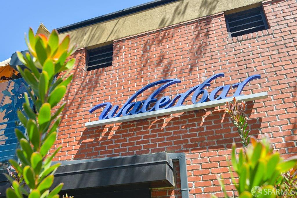 Brick building facade with a blue Waterbar sign and leafy plants in the foreground.
