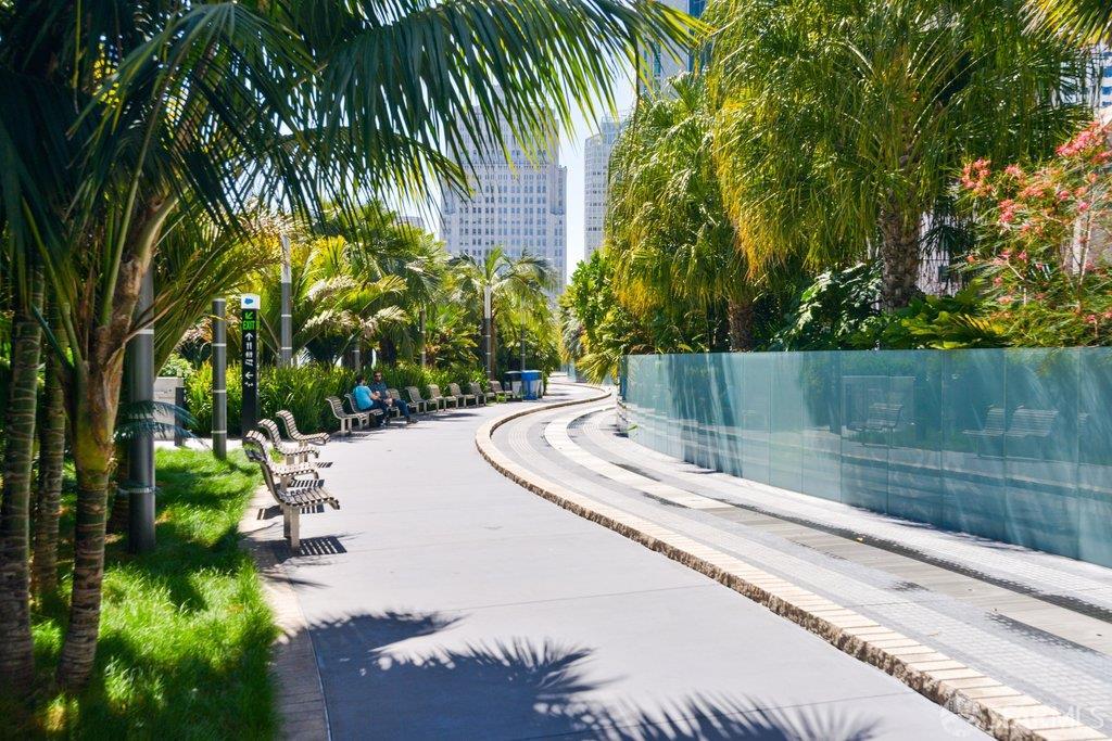 Curving urban walkway lined with palm trees and benches beside a glass railing.