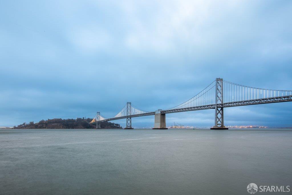 San Francisco Bay and the Bay Bridge beneath a cloudy blue sky.
