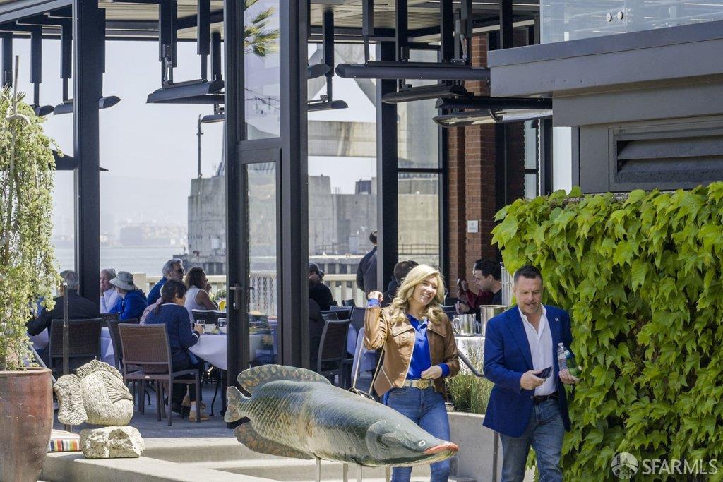 Outdoor patio with glass walls, leafy greenery, and a large fish sculpture in the foreground.