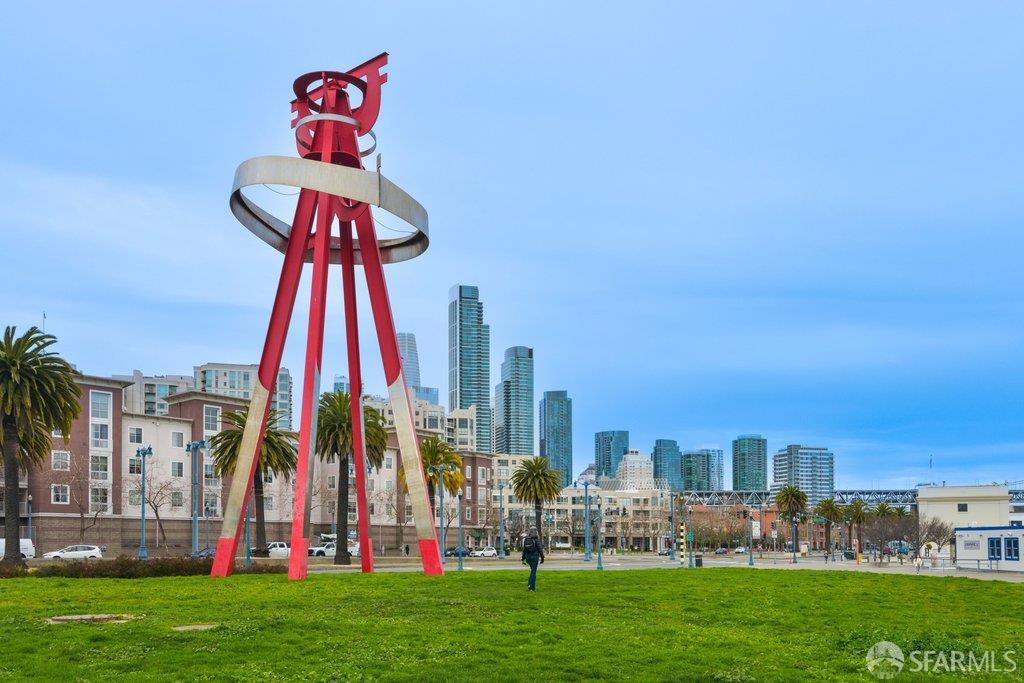 Red-and-silver abstract sculpture in a San Francisco park, with downtown towers behind it.
