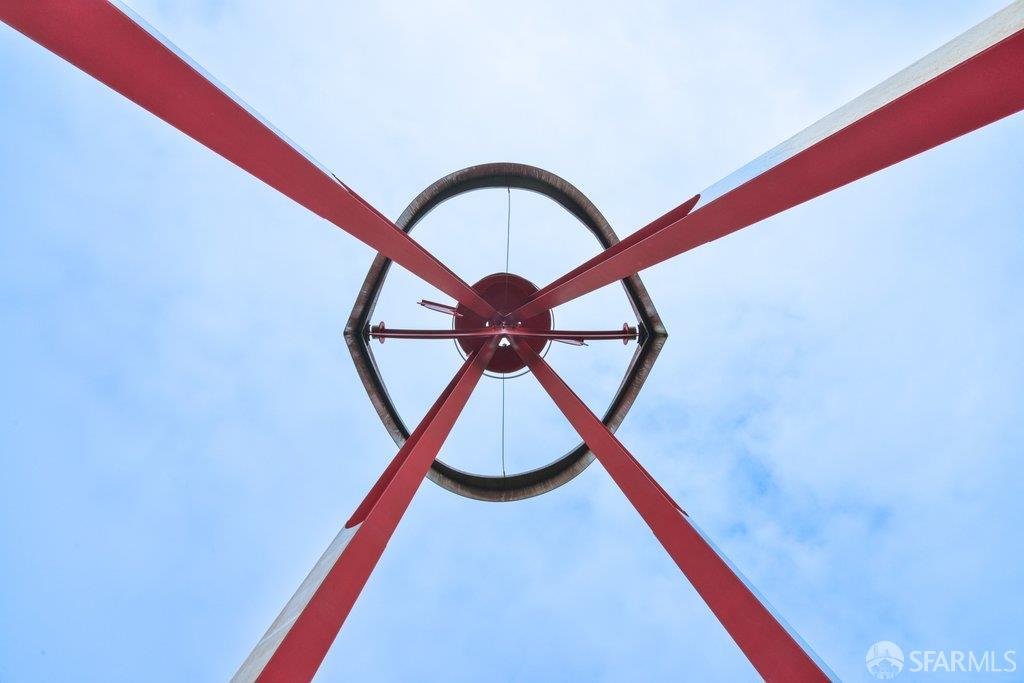 Red metal beams cross through a circular ring overhead against a blue sky.