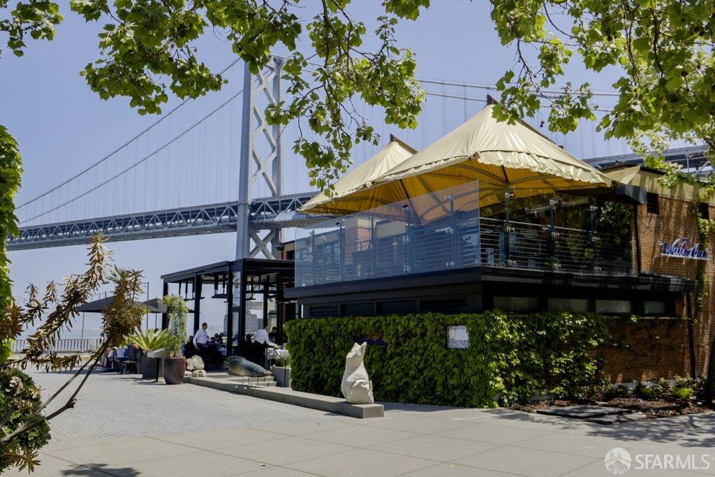 Waterfront restaurant terrace beneath a cream canopy, with the Bay Bridge in the background.