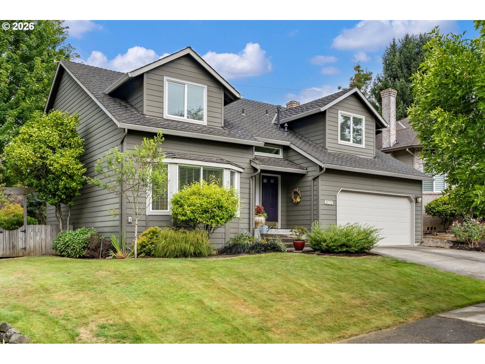 Gray two-story house with an attached garage, landscaped front yard, and driveway.