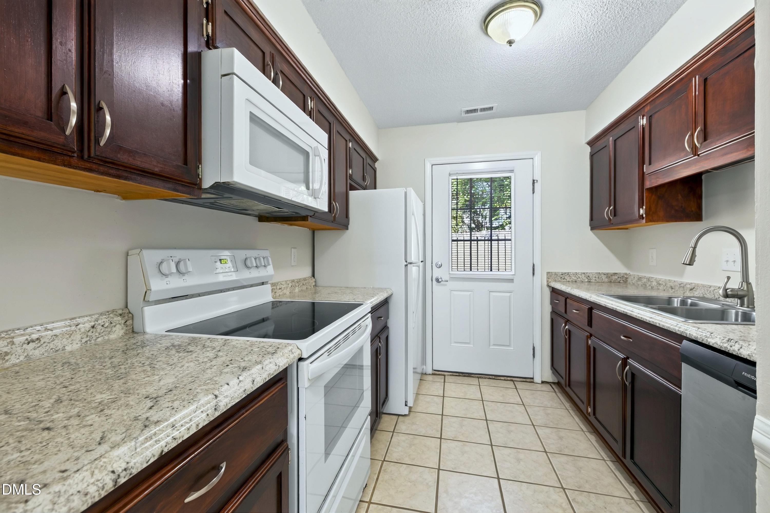Galley kitchen with dark wood cabinets, granite counters, white appliances, and a glass-panel back door.