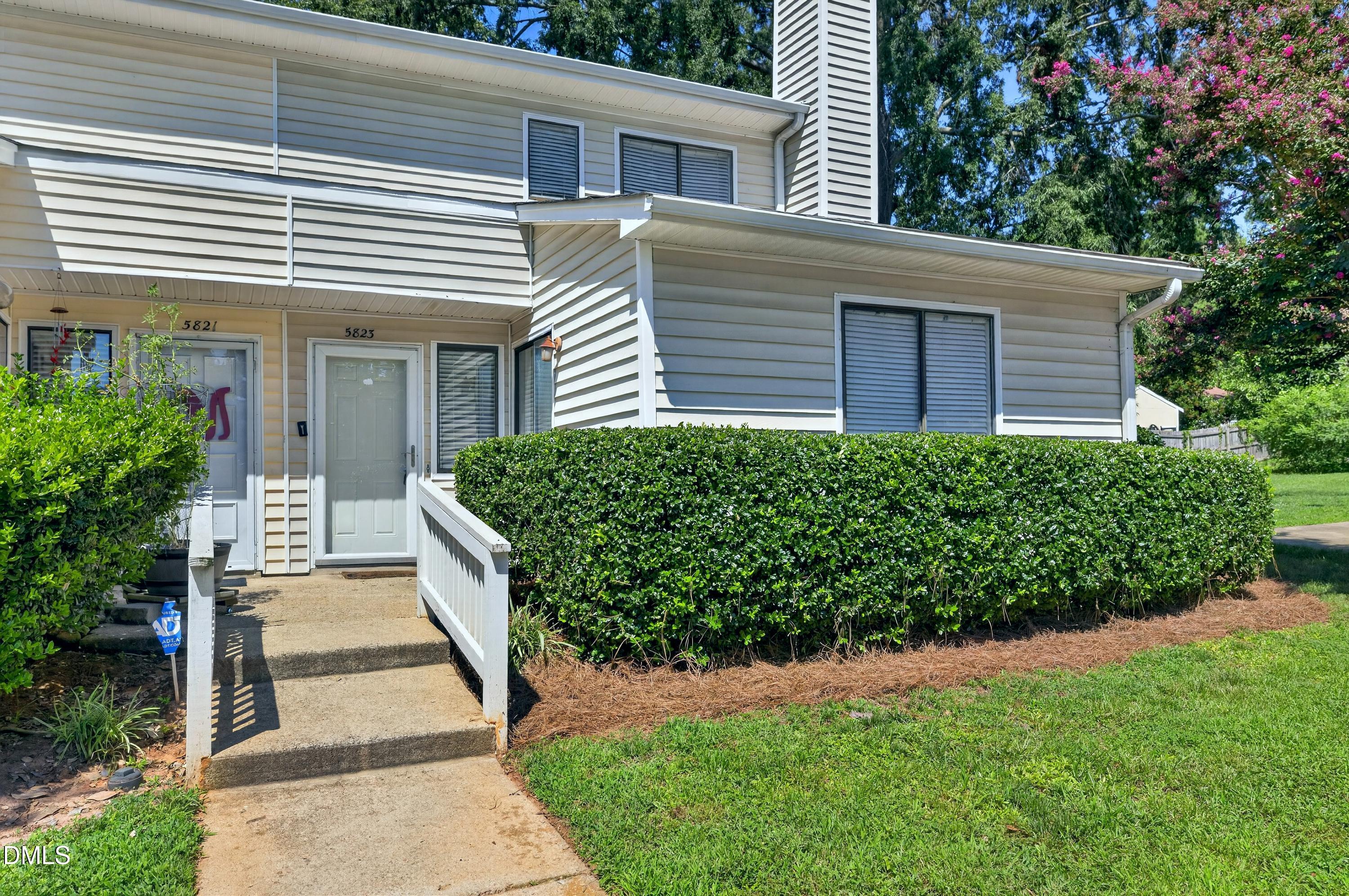 Two-story residence entrance with a concrete walkway, white railing, and neatly trimmed hedges.