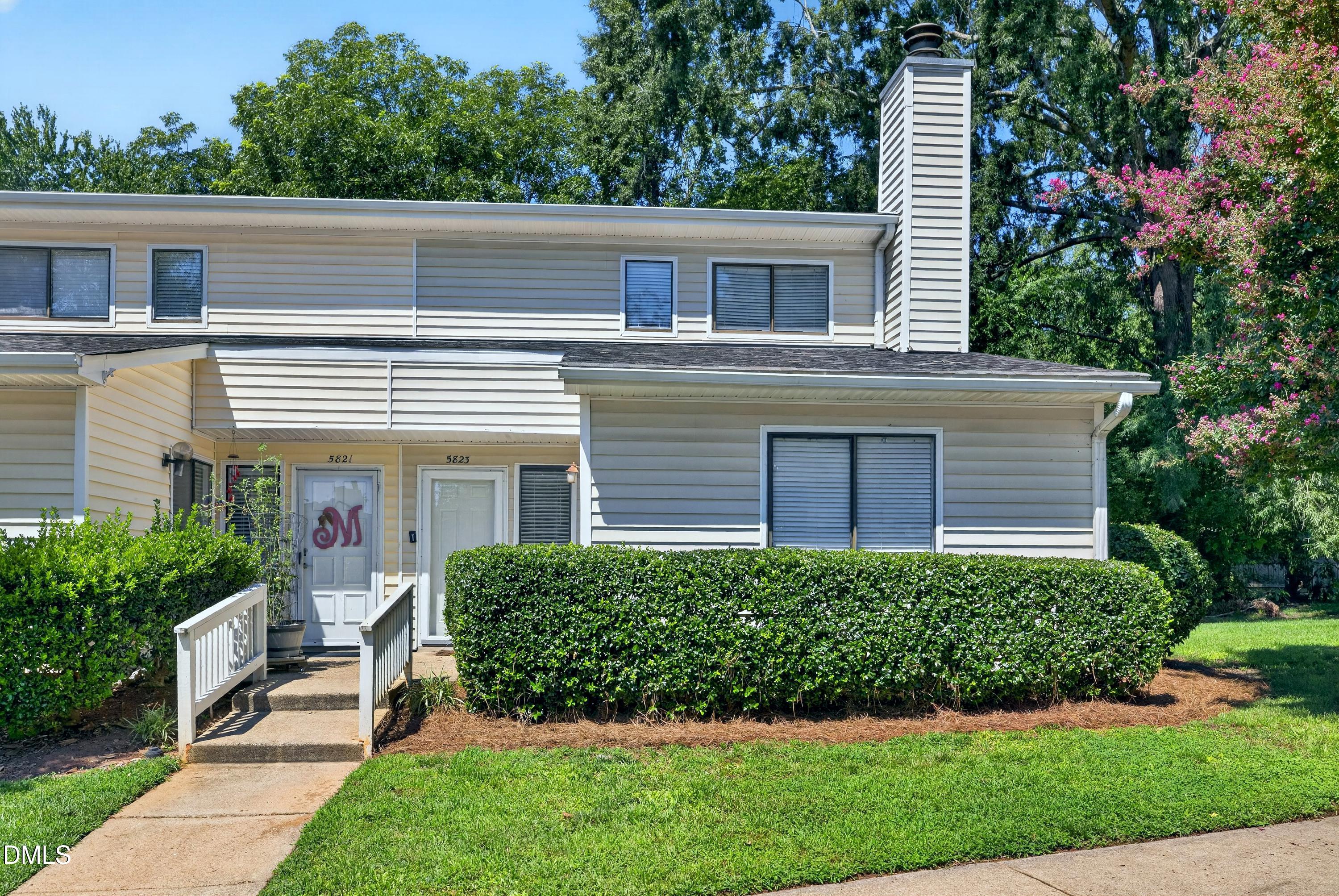 Two-story gray-sided home with white entry ramp, clipped hedges, and a flowering tree.