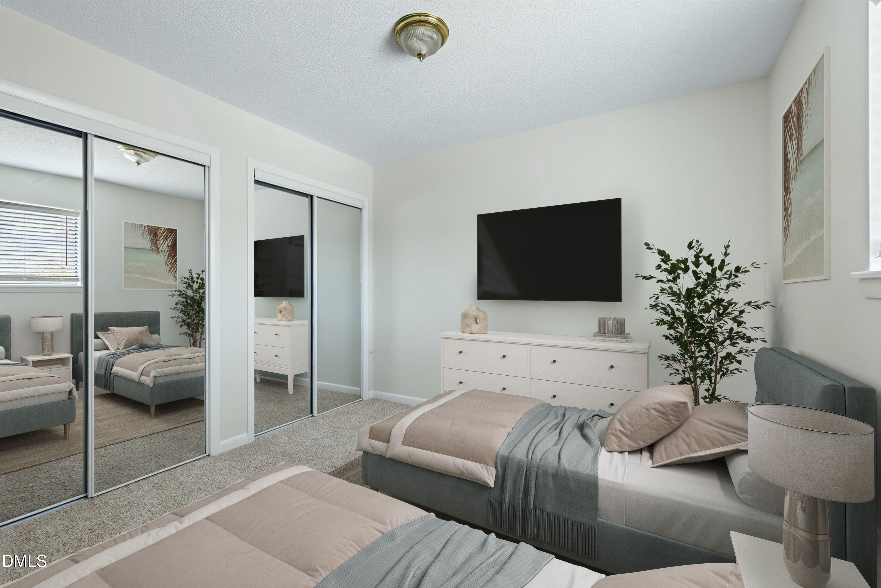 Staged bedroom with two beds, mirrored closet doors, and a wall-mounted TV.