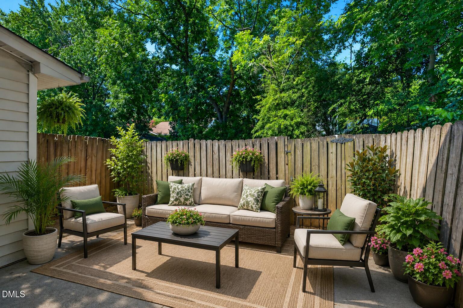 Furnished backyard patio with wicker seating, potted flowers, and a tall wooden privacy fence.