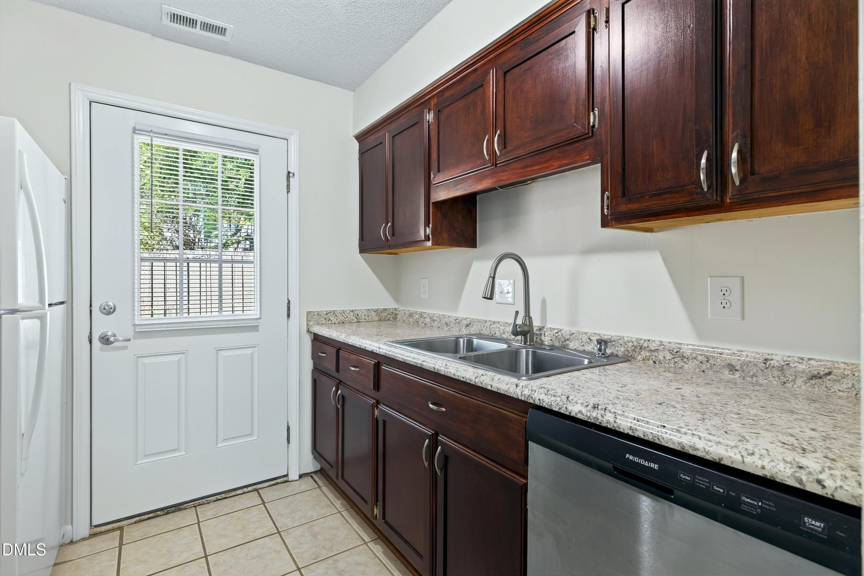 Kitchen with dark cherry cabinets, speckled stone counters, a double-basin sink, and a windowed exterior door.