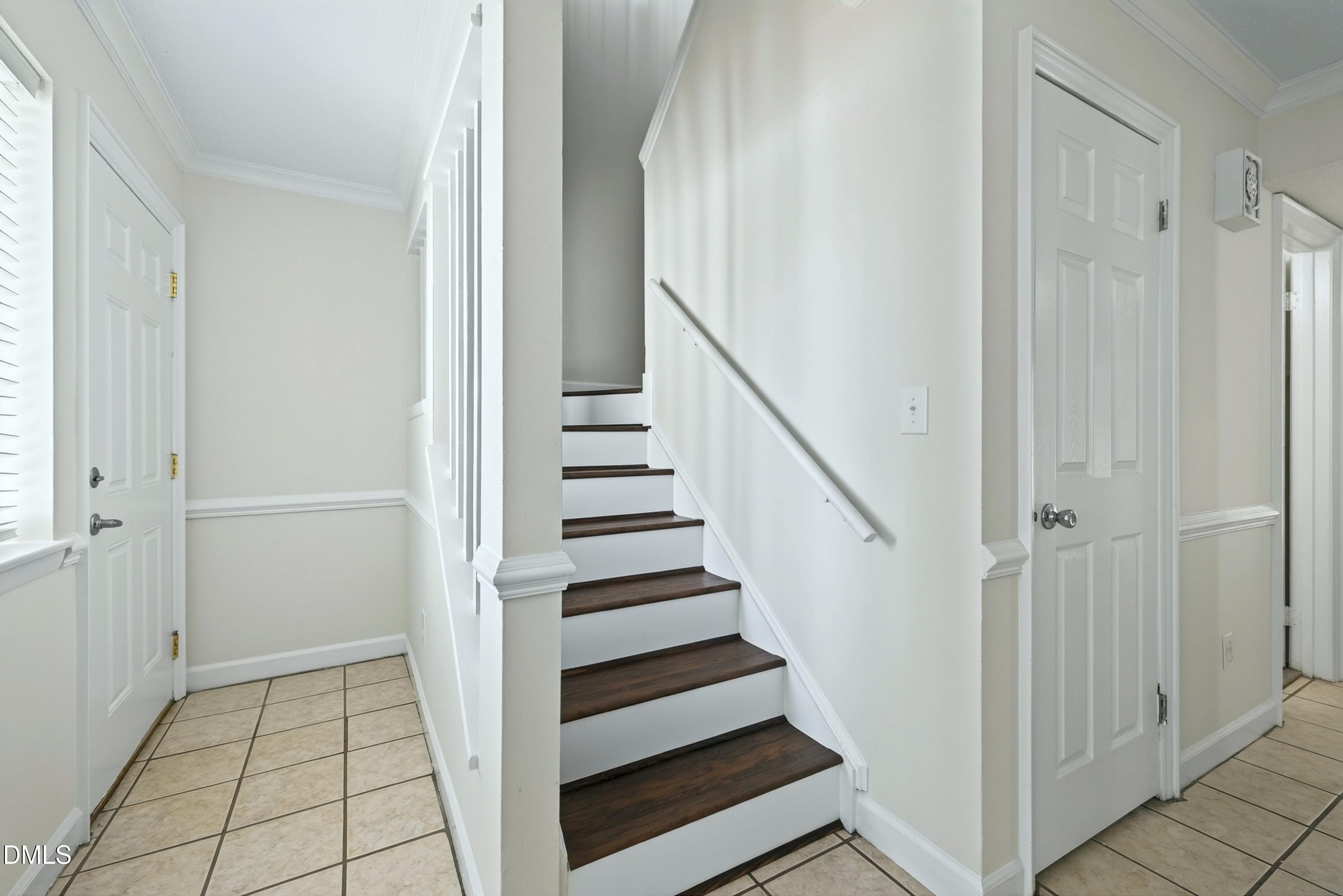 Entry hall with a dark-tread staircase, beige tile floor, and white paneled doors.