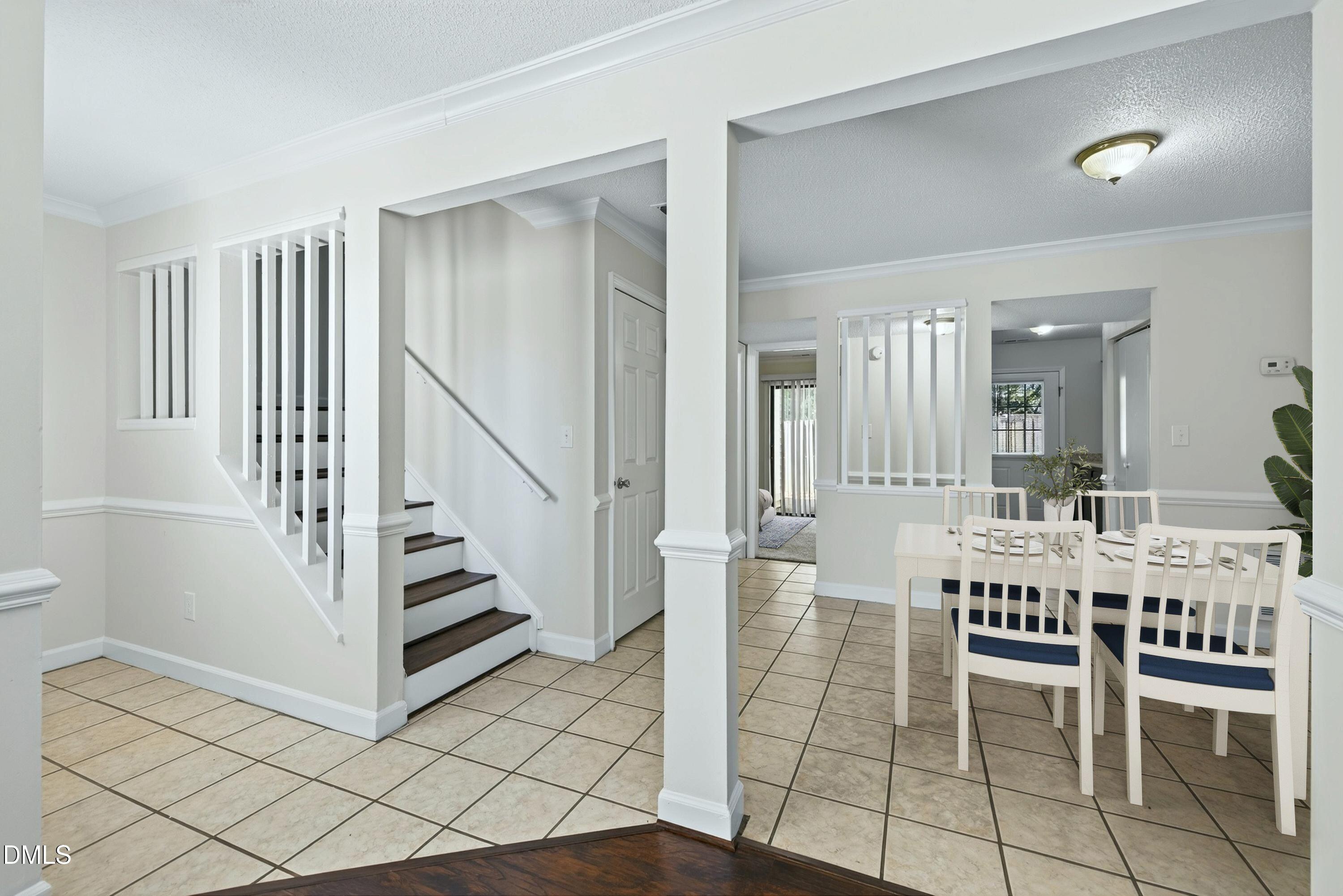 Dining area with white table and chairs beside a tiled foyer and staircase.