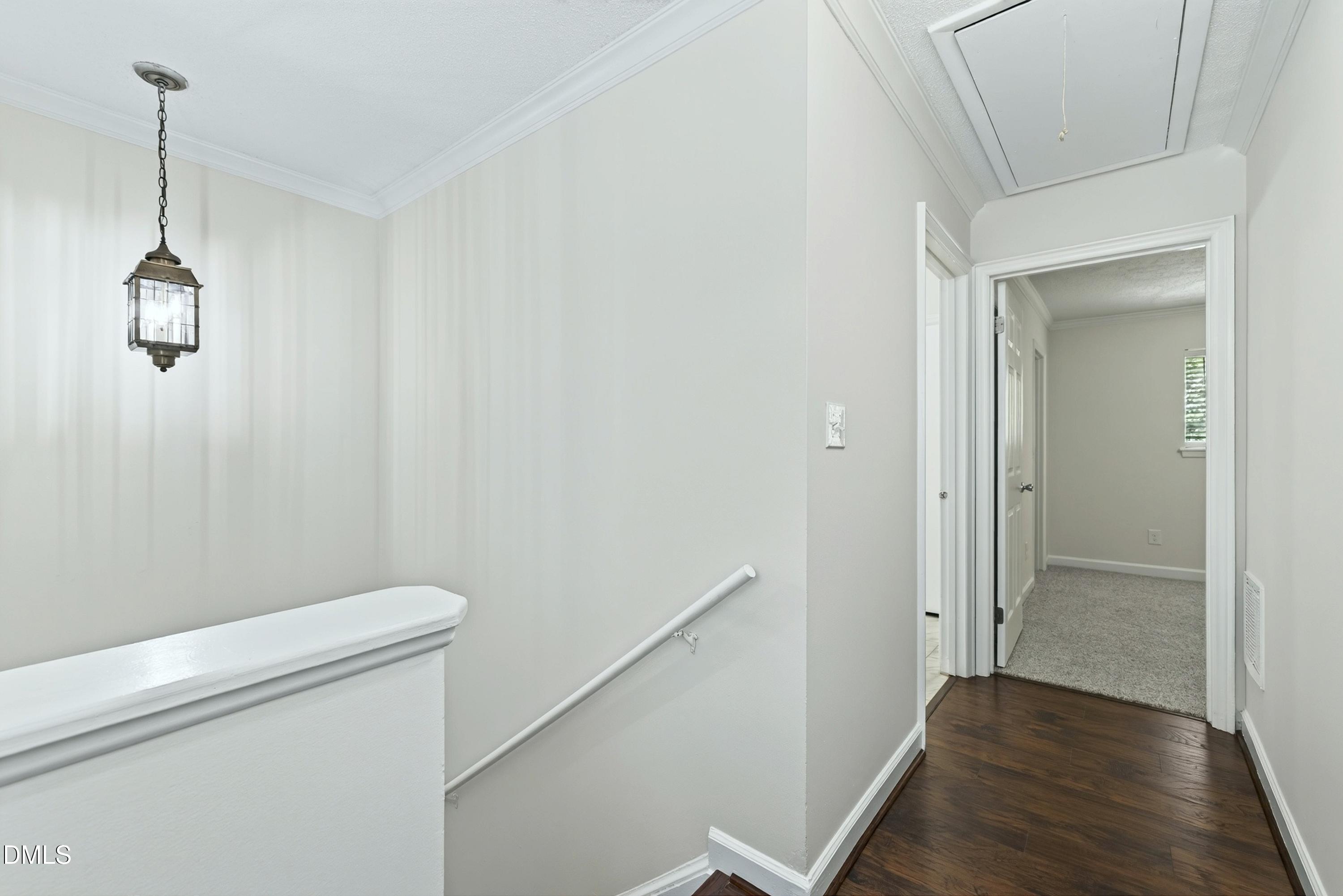 Hallway and stair landing with dark hardwood floors, a hanging lantern, and an open doorway to a carpeted room.