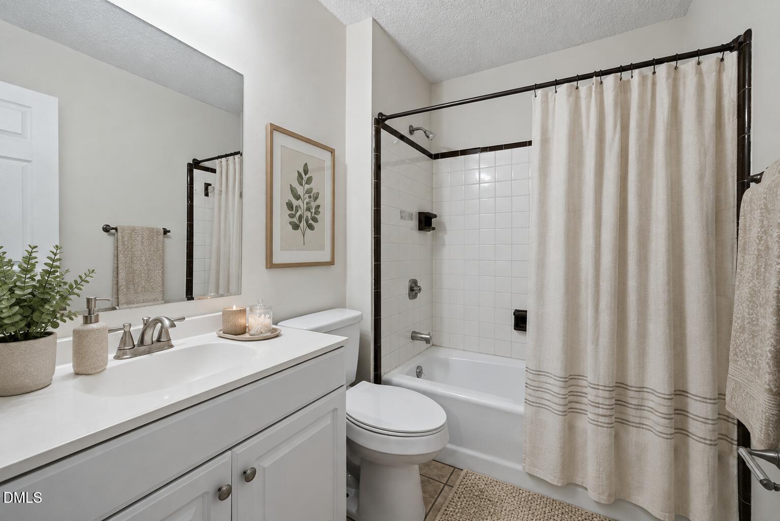 Bathroom with a white vanity and tiled tub-shower behind a beige curtain.