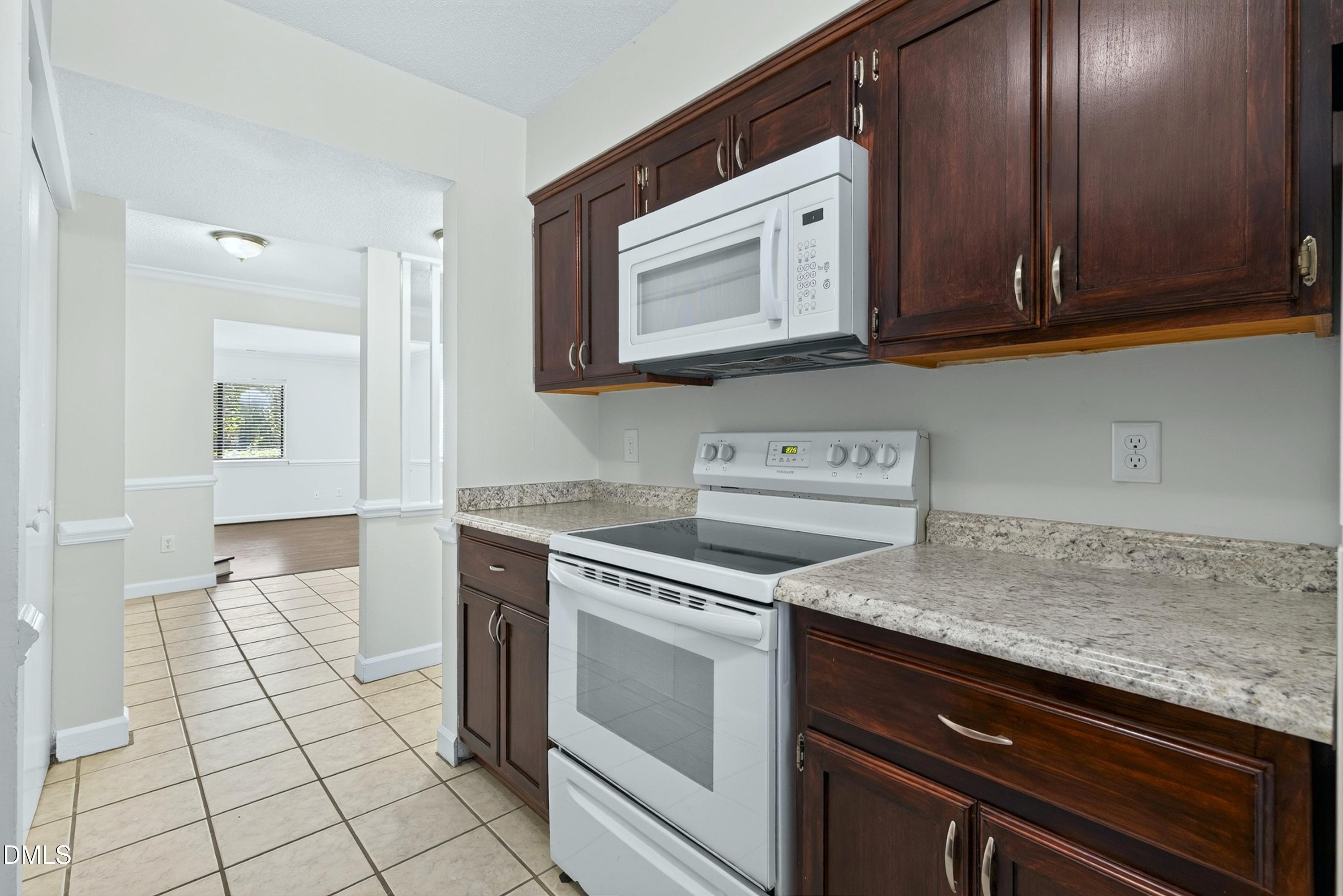 Kitchen with dark wood cabinets, stone-pattern counters, and white range and microwave.