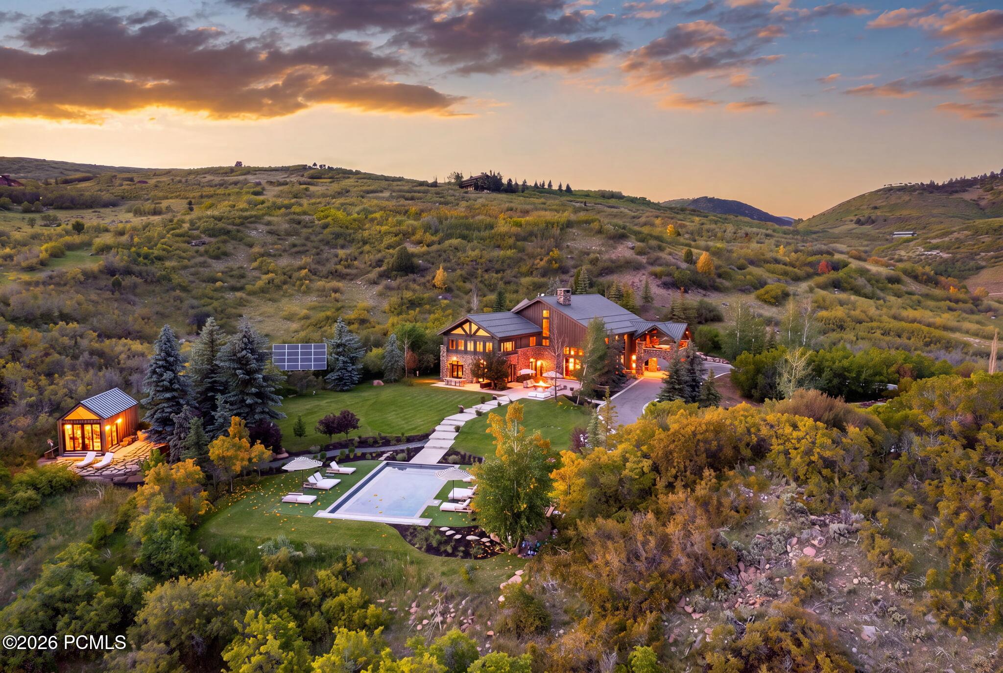 Aerial view of a mountain home with a pool, detached cabin, and autumn hills.