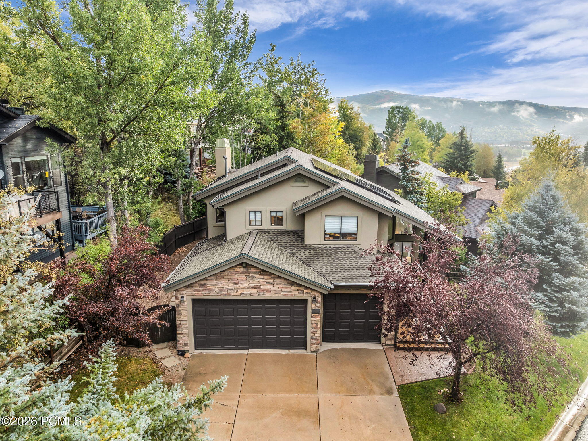 Jeremy Ranch home with a stone facade, two garage doors, and mountain views beyond the trees.