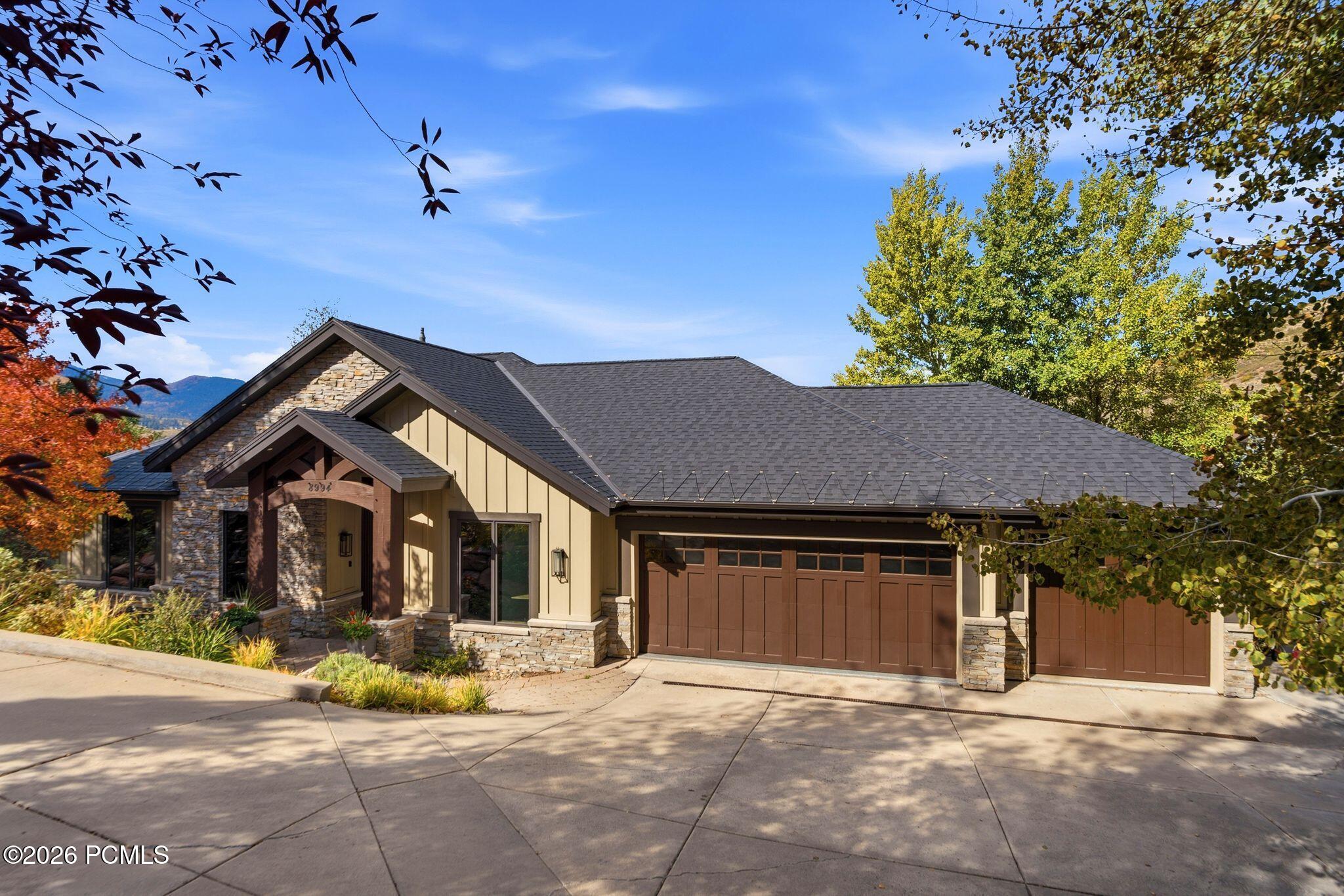 Single-story stone-and-siding home with two brown garage doors, framed by autumn trees and a distant mountain.