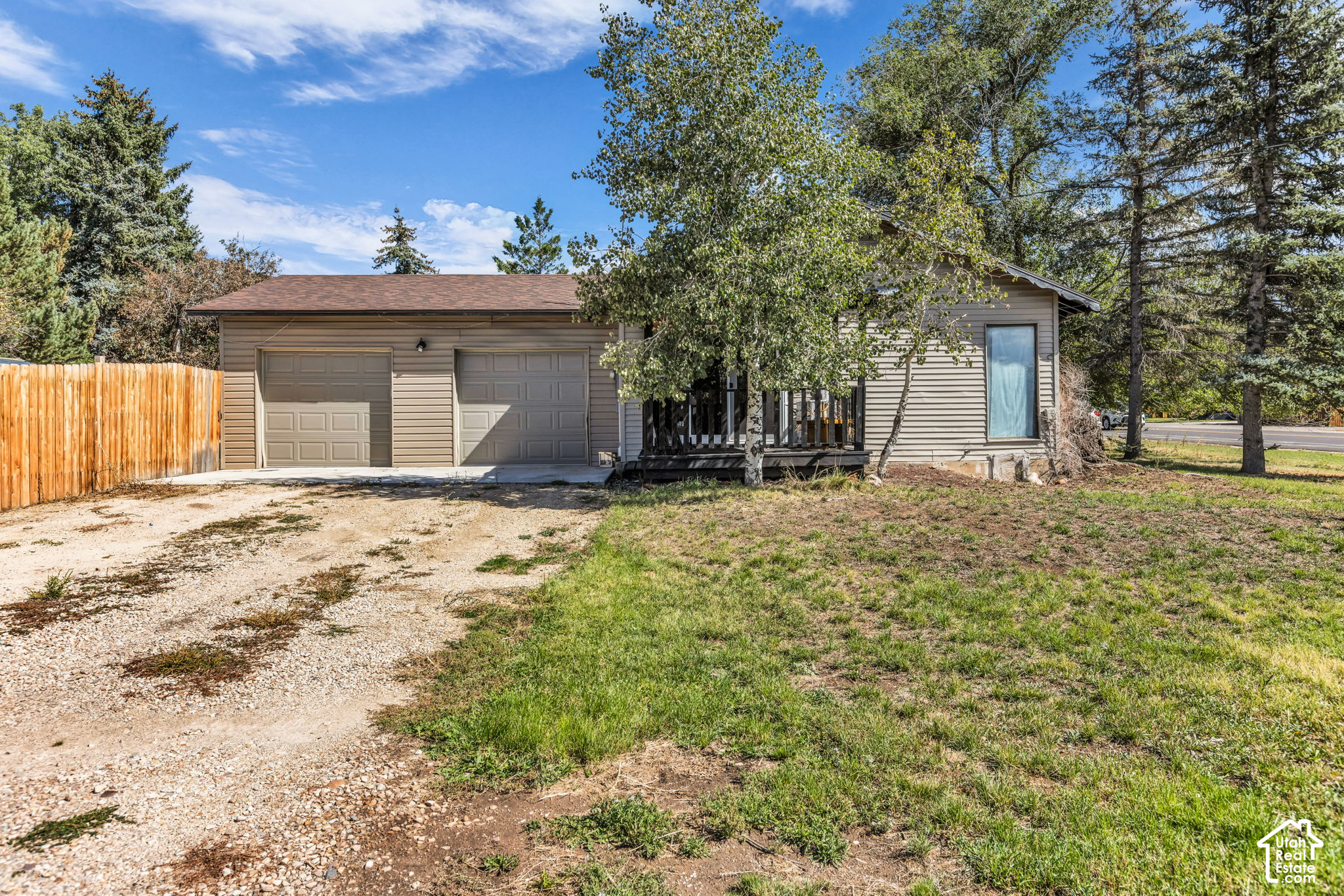 Single-story beige house with two garage doors, a covered porch, and a gravel driveway.