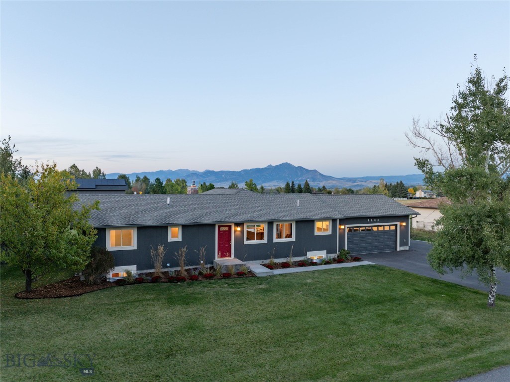 Single-story dark gray home with a red door, attached garage, and mountain views.