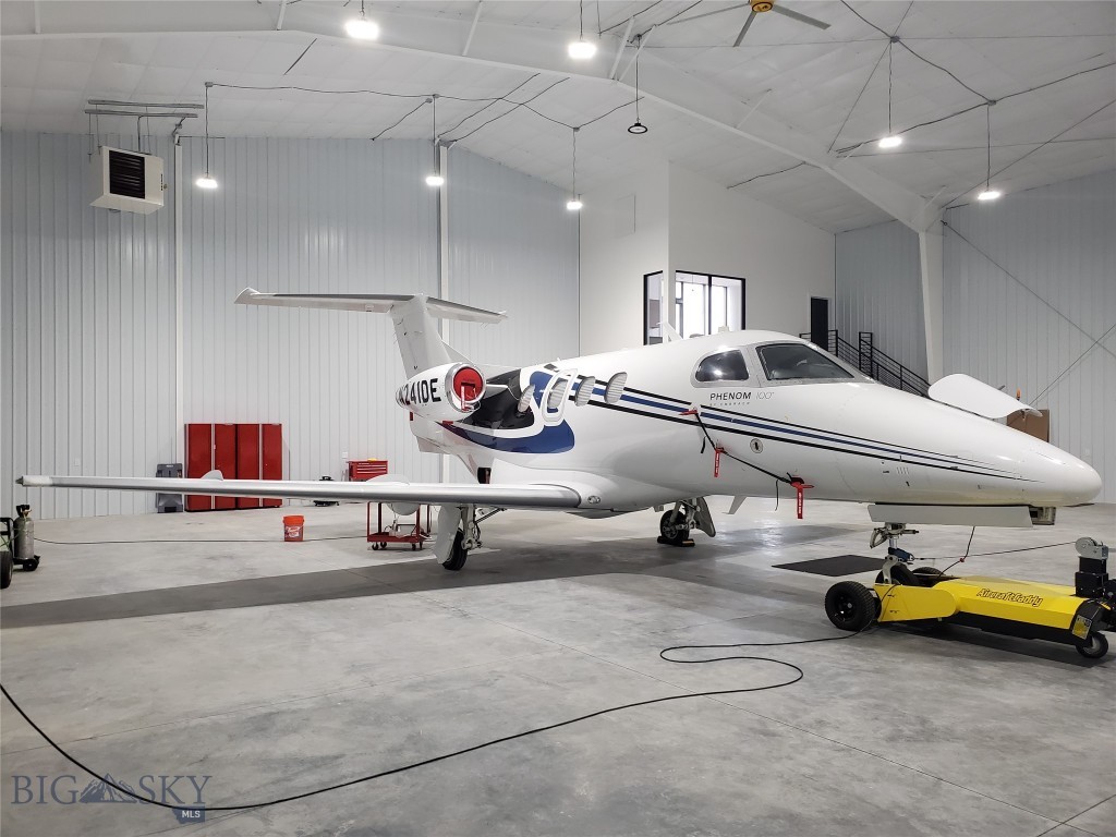 Private jet inside a bright hangar, with a yellow aircraft tug beside it.