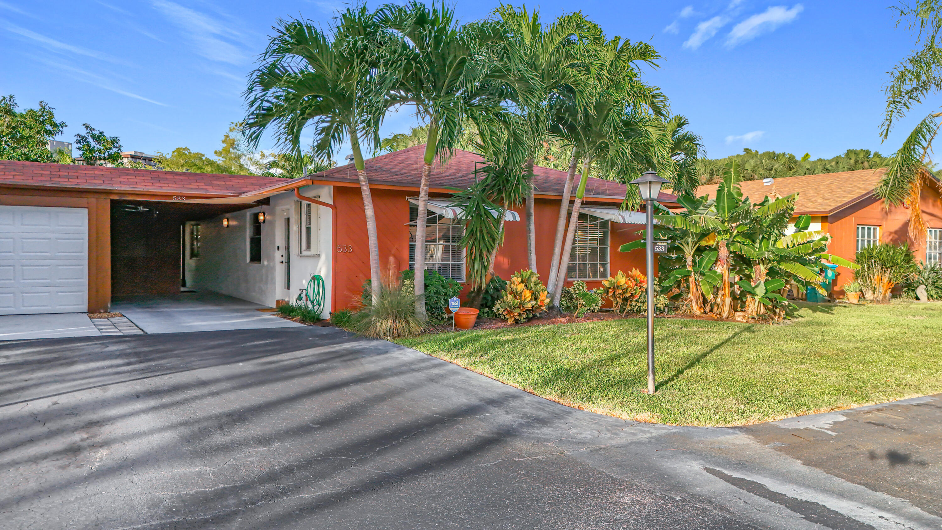 Single-story red-orange home with an attached garage, palm trees, and tropical landscaping.