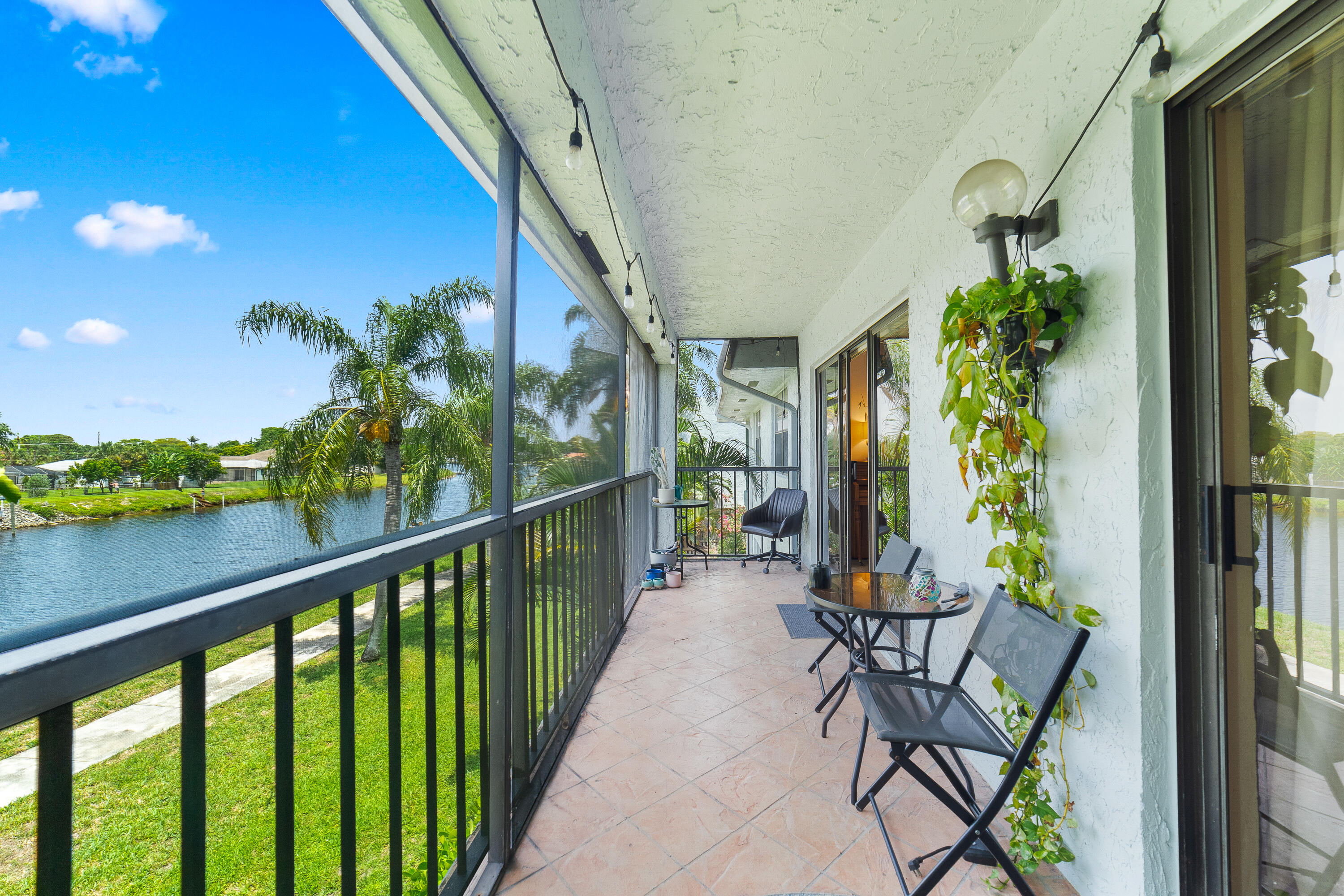 Screened balcony with patio seating overlooking a canal and palm trees.