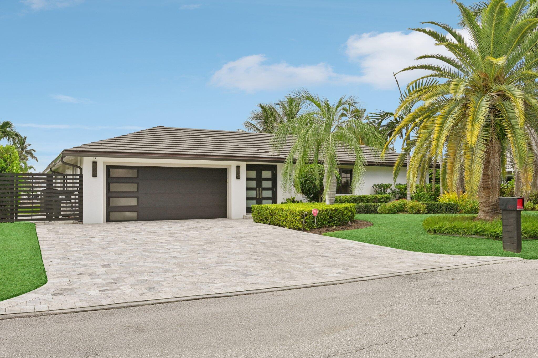 Modern white home with a broad dark garage, paved driveway, and palm trees.