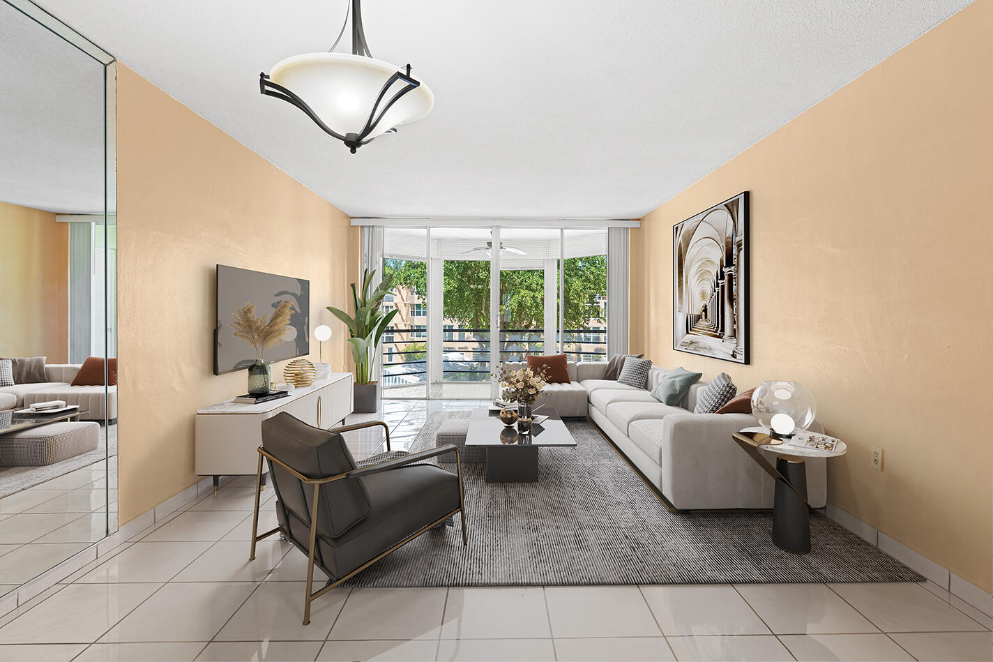 Staged condo living room with a white sectional and sliding glass doors overlooking a leafy balcony.