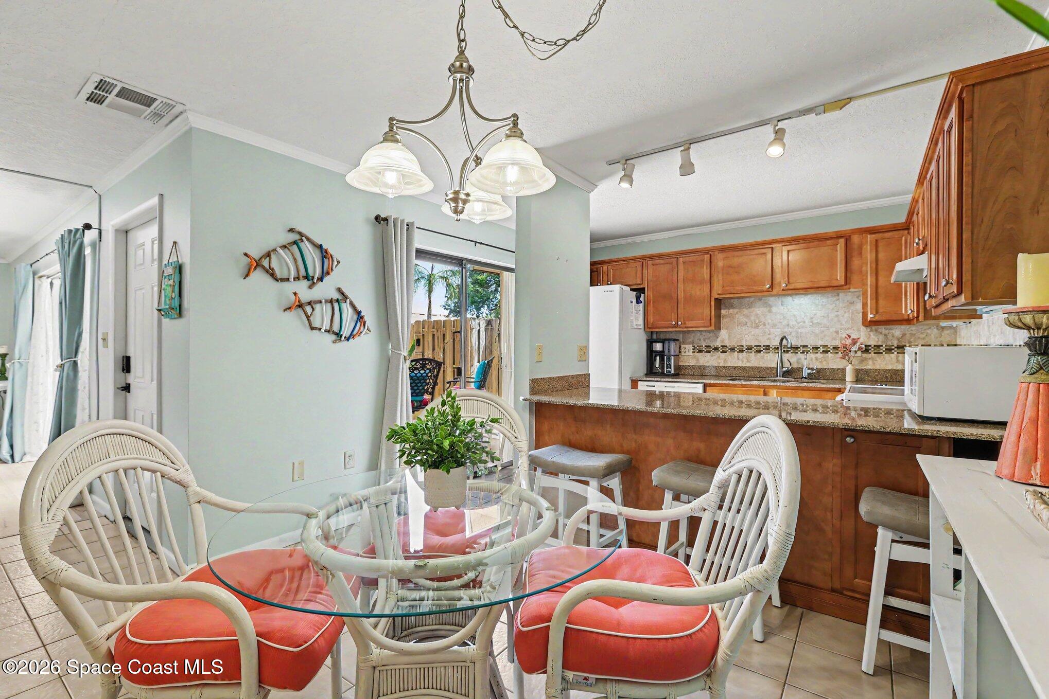 Kitchen and dining area with wood cabinets, a granite breakfast bar, and white wicker chairs with coral cushions.