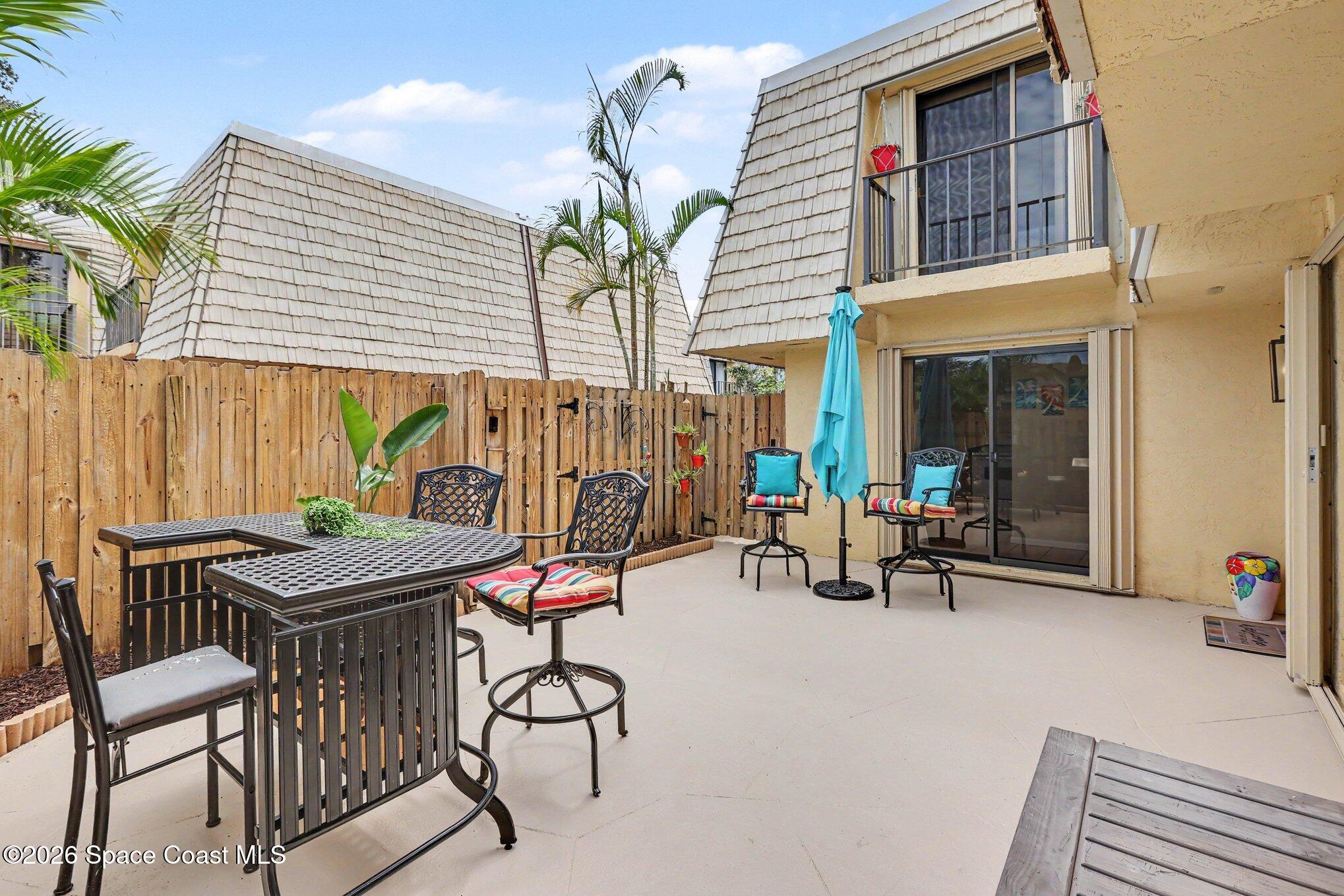 Furnished patio with black metal seating, turquoise umbrella, wooden privacy fence, and sliding glass doors.