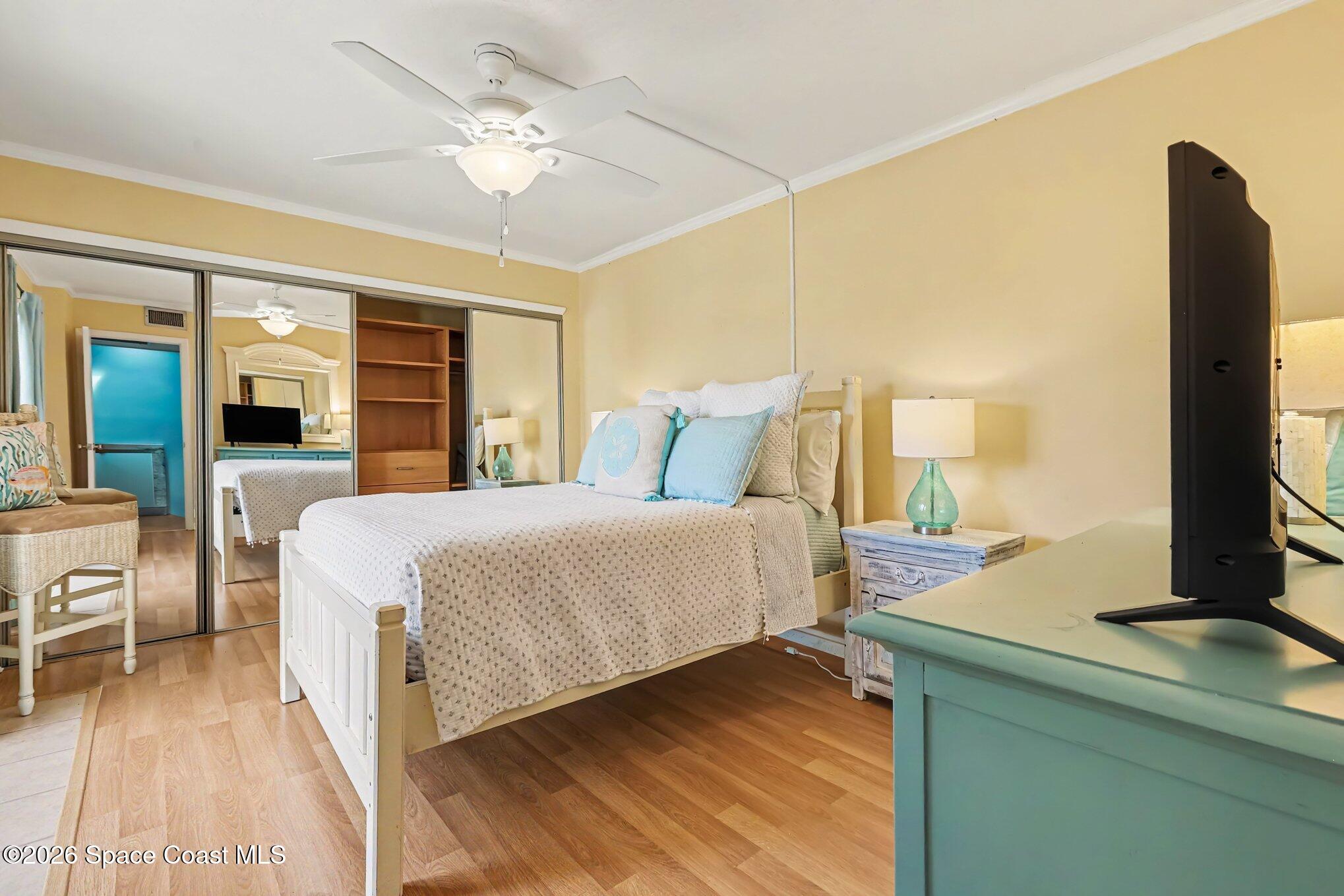 Bedroom with a white bed, mirrored closet doors, and a turquoise dresser with a television.