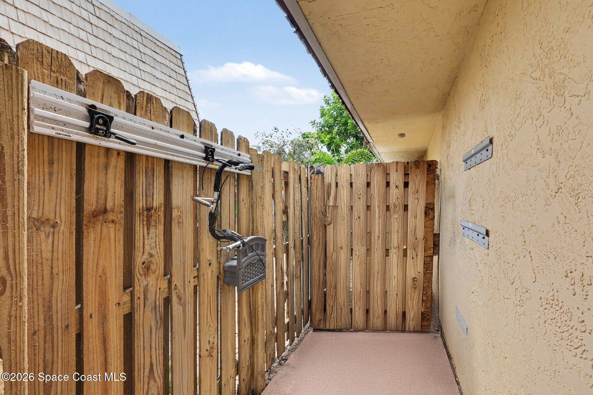 Covered side patio with a wooden privacy fence and a bicycle hanging from a rack.