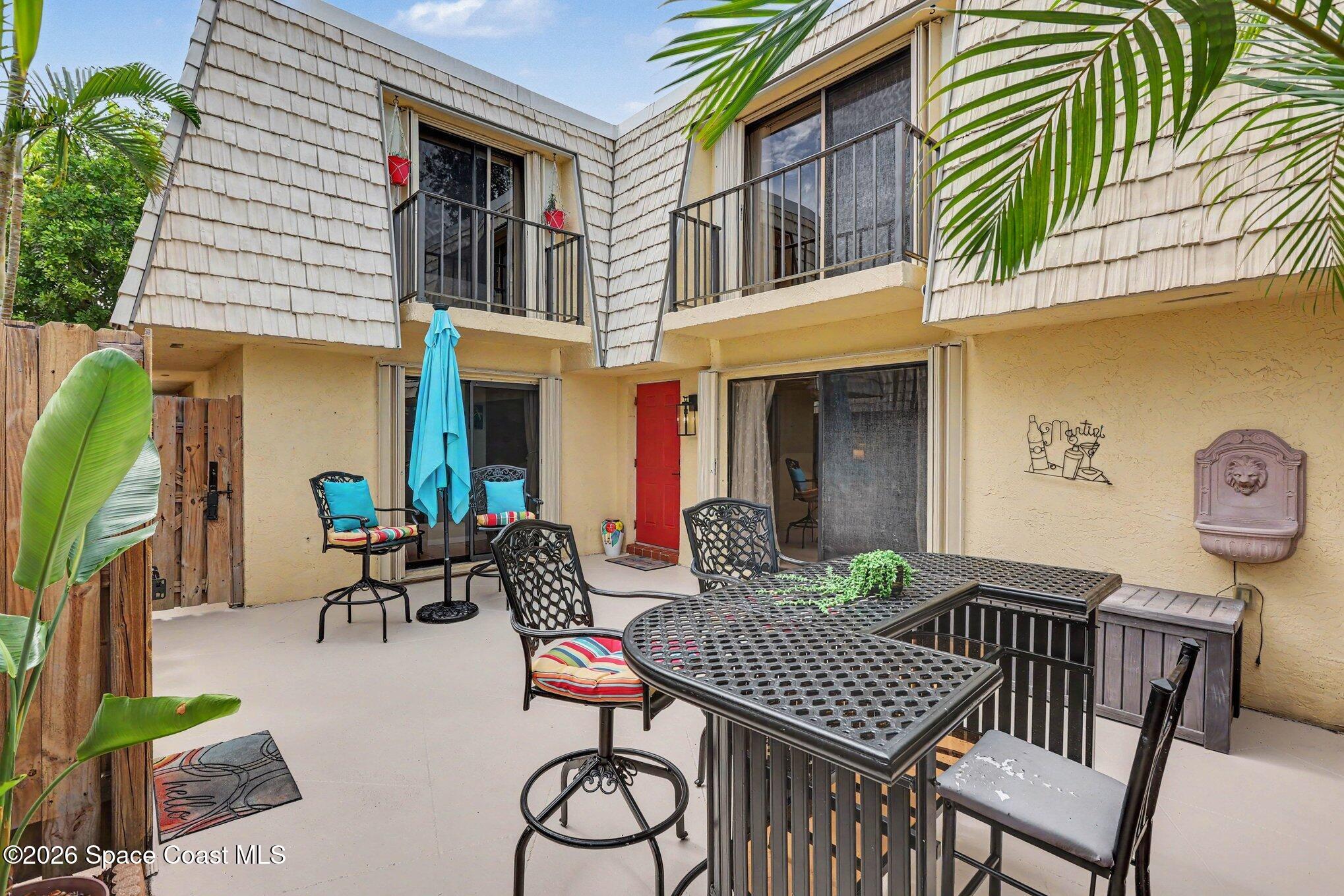 Condo patio with metal dining set, turquoise umbrella, red door, and upper-level balconies.