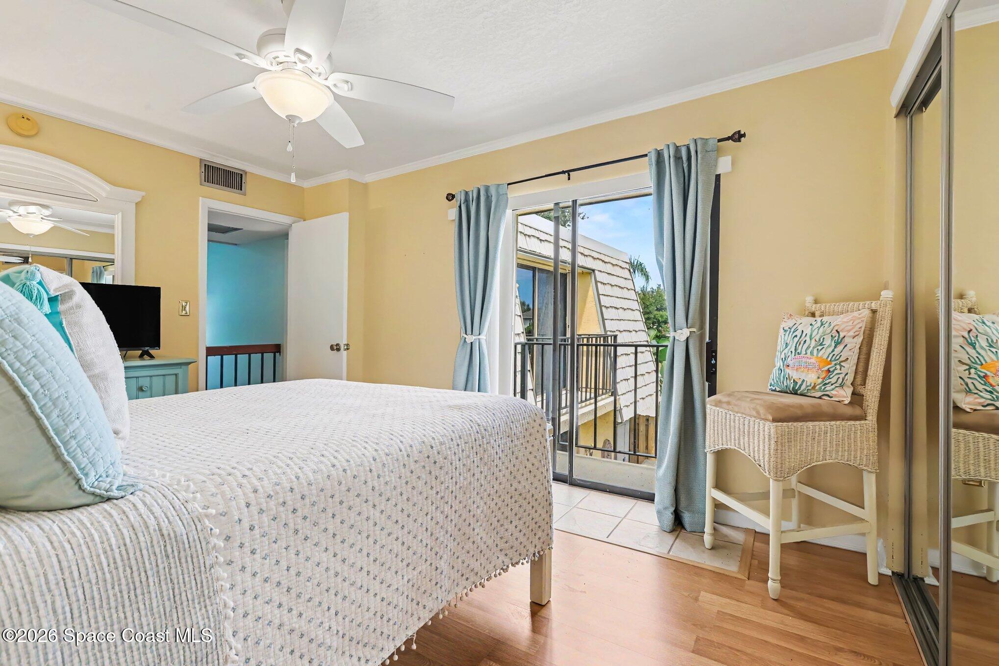 Bedroom with a white quilted bed, wicker chair, and sliding glass doors to a balcony.