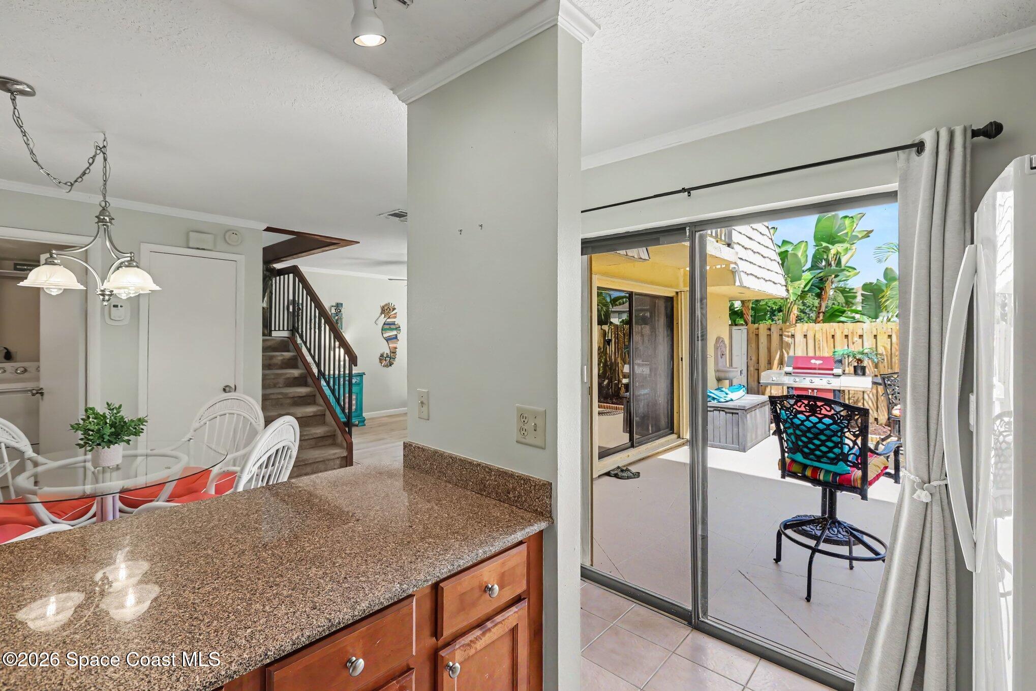Kitchen and dining area opening onto a tiled patio with a grill and fenced tropical yard.