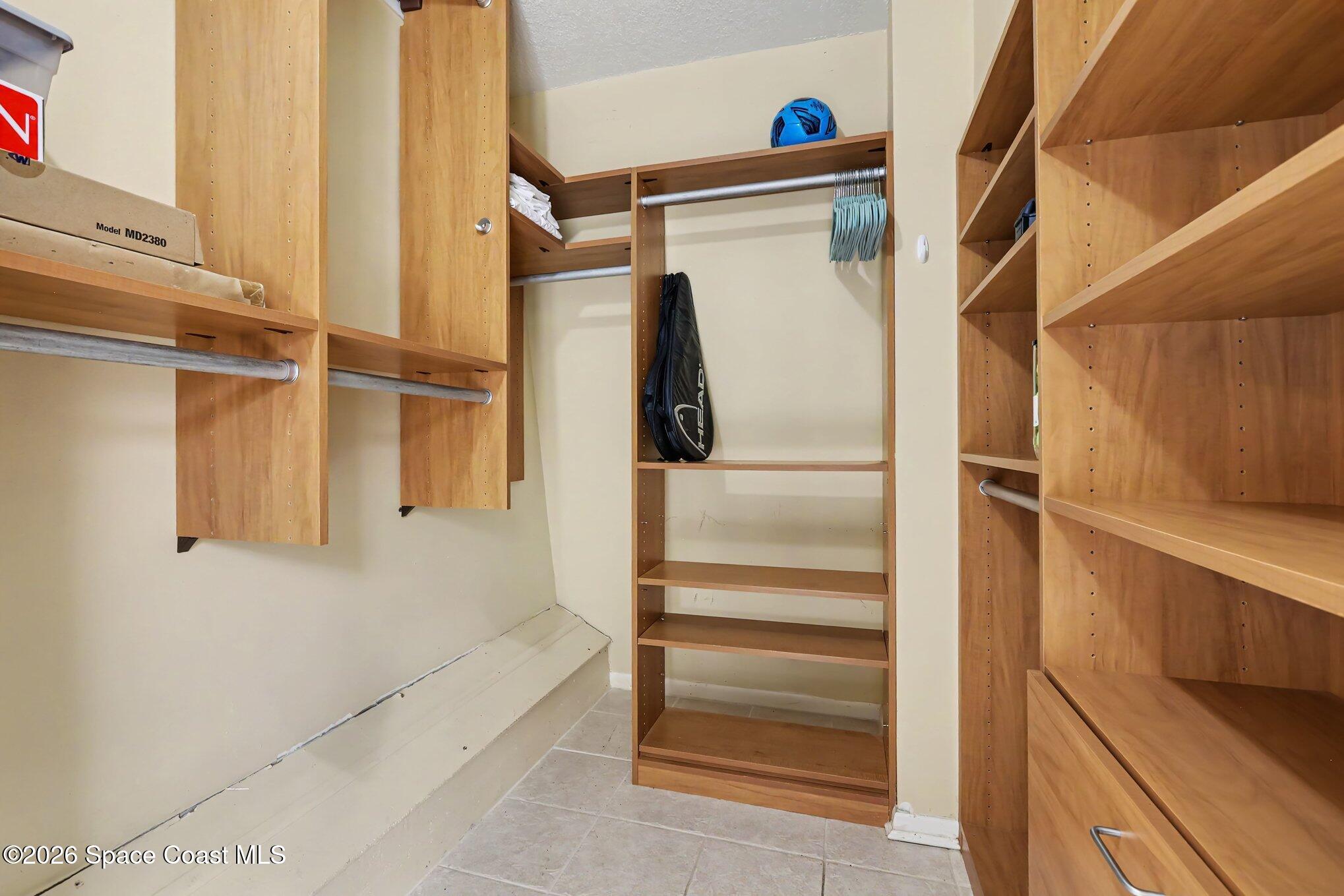 Walk-in closet with built-in wood shelving, hanging rods, and tiled floor.