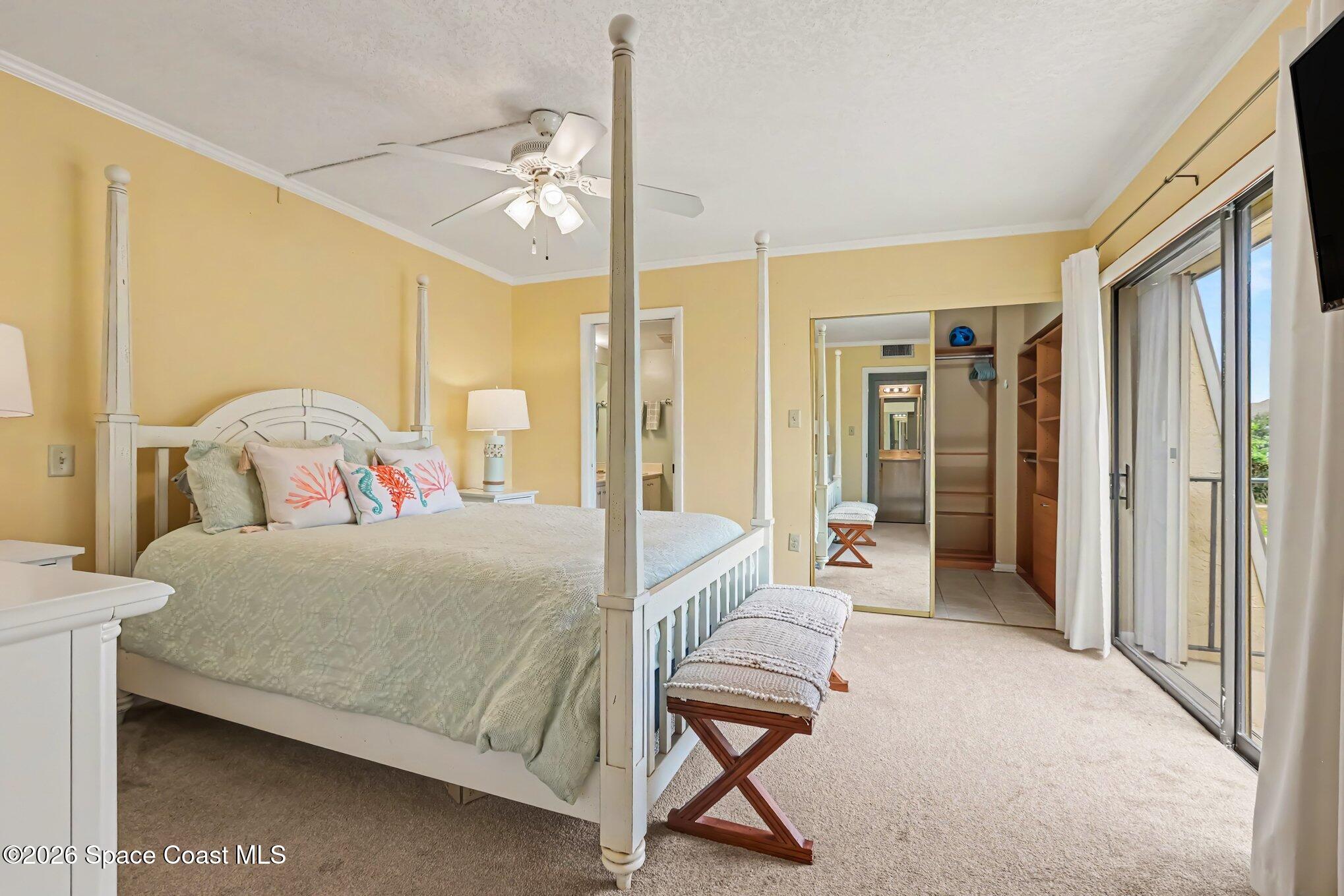 Bedroom with a white four-poster bed, coral-print pillows, mirrored closets, and sliding glass doors to a balcony.