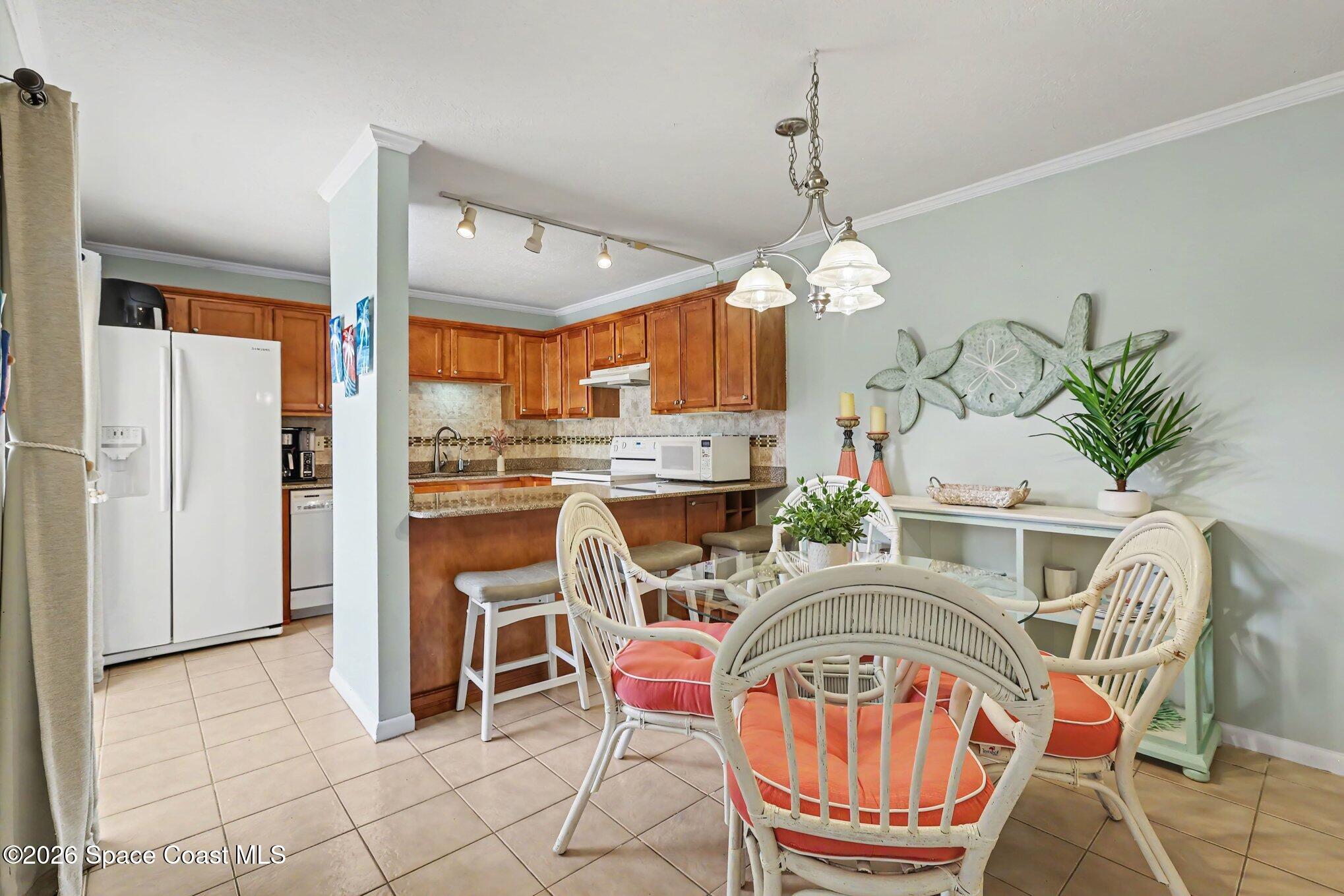 Kitchen and dining area with wood cabinets, glass table, and white wicker chairs with coral cushions.