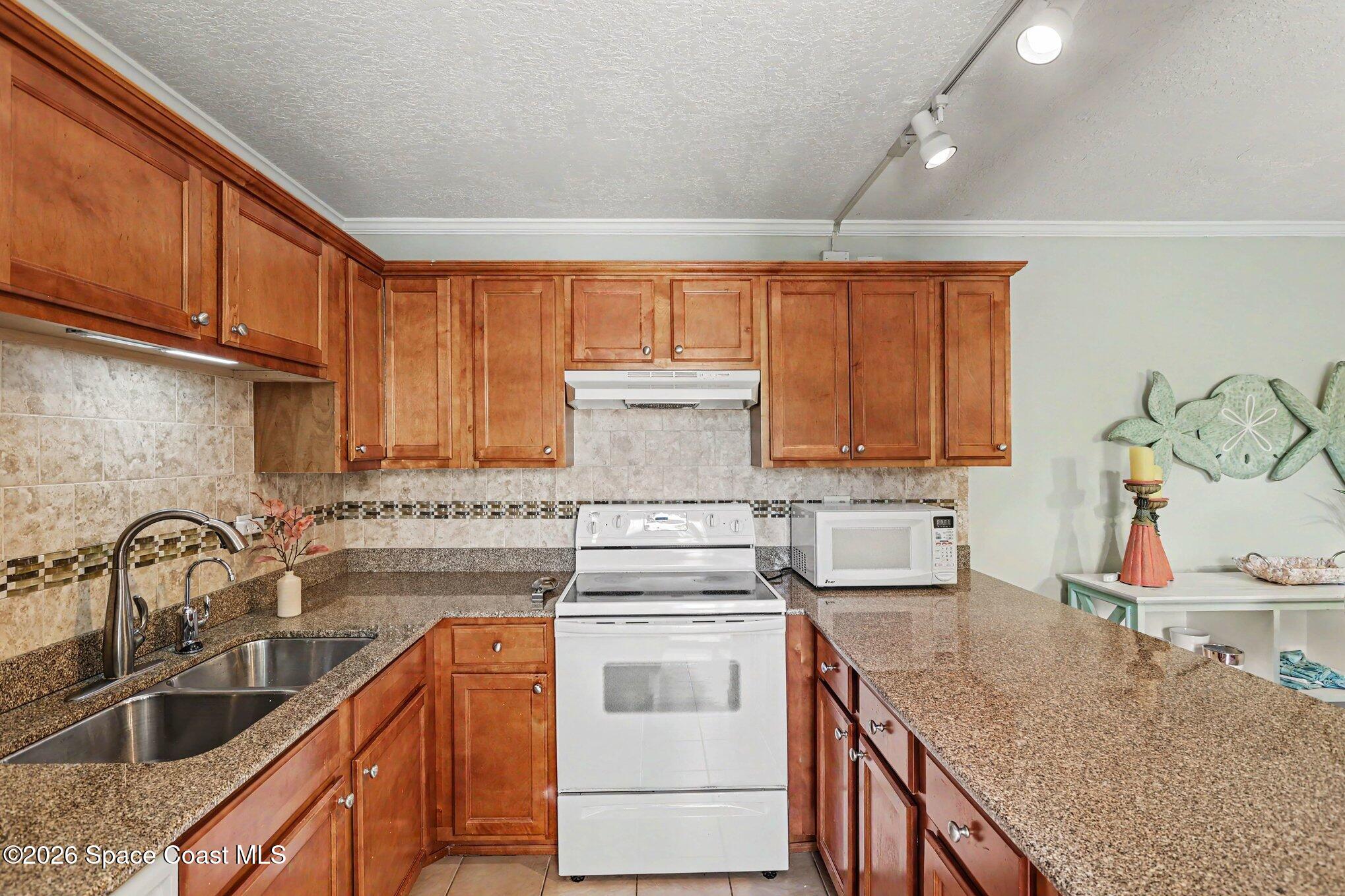 Kitchen with warm wood cabinets, granite counters, a double sink, and white appliances.