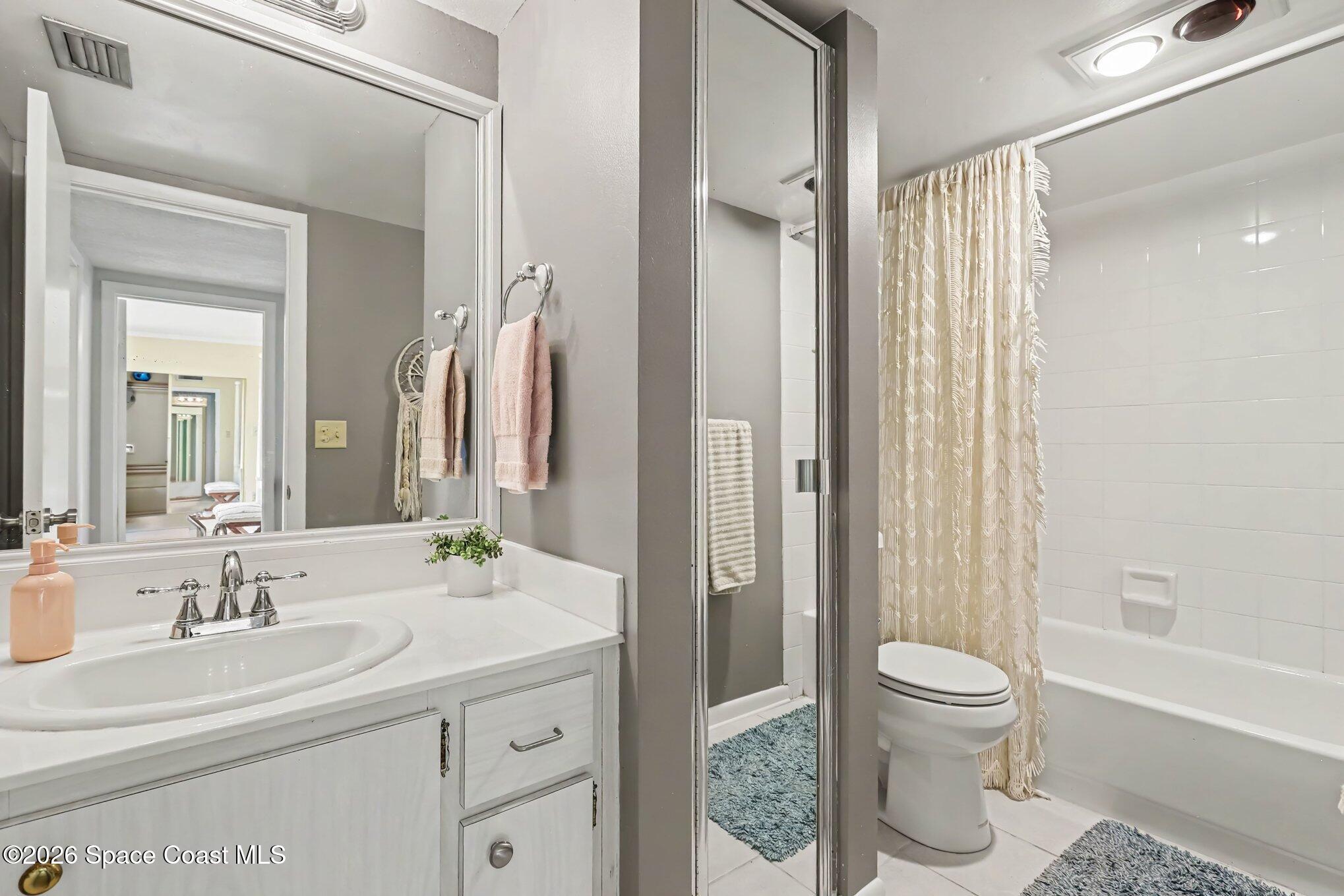 Bathroom with white vanity, large mirror, toilet, and bathtub behind a cream patterned shower curtain.