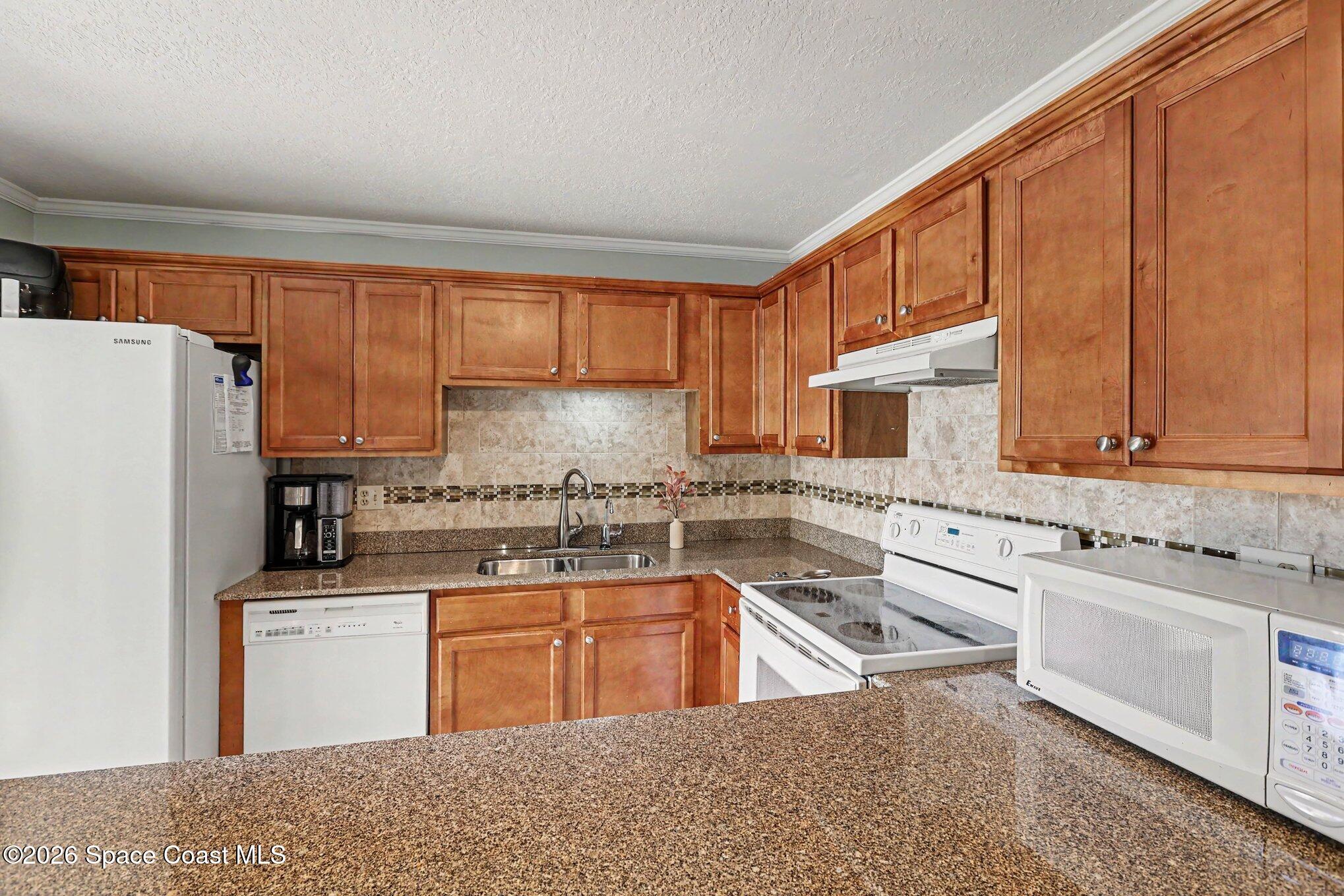 Kitchen with warm wood cabinets, granite counters, tiled backsplash, and white appliances.