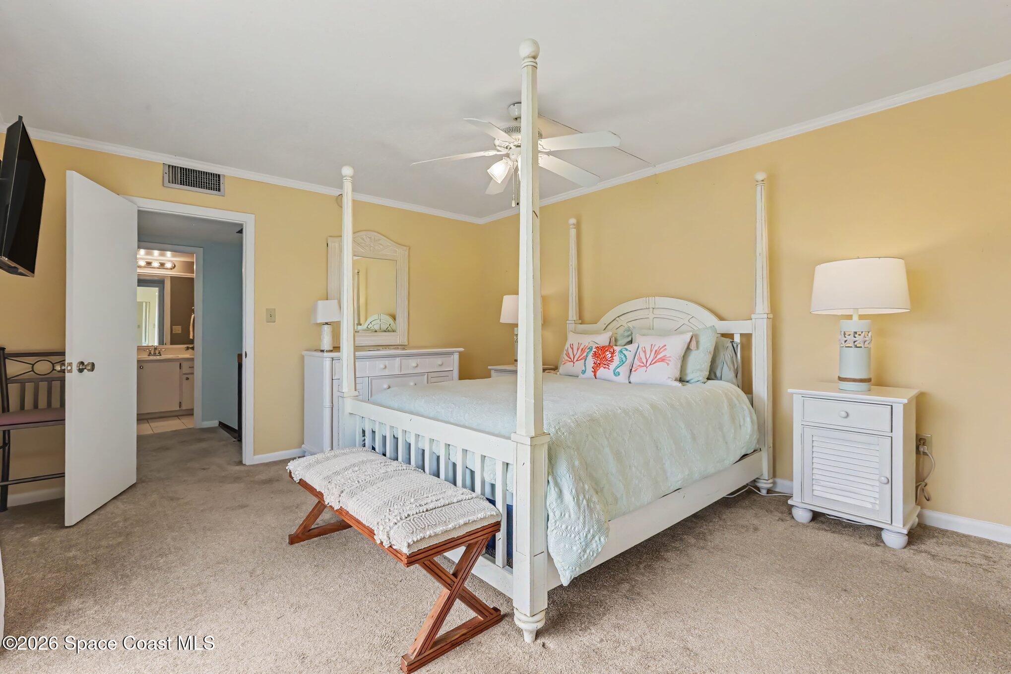 Bedroom with a white four-poster bed, coral-patterned pillows, and an adjoining bathroom doorway.
