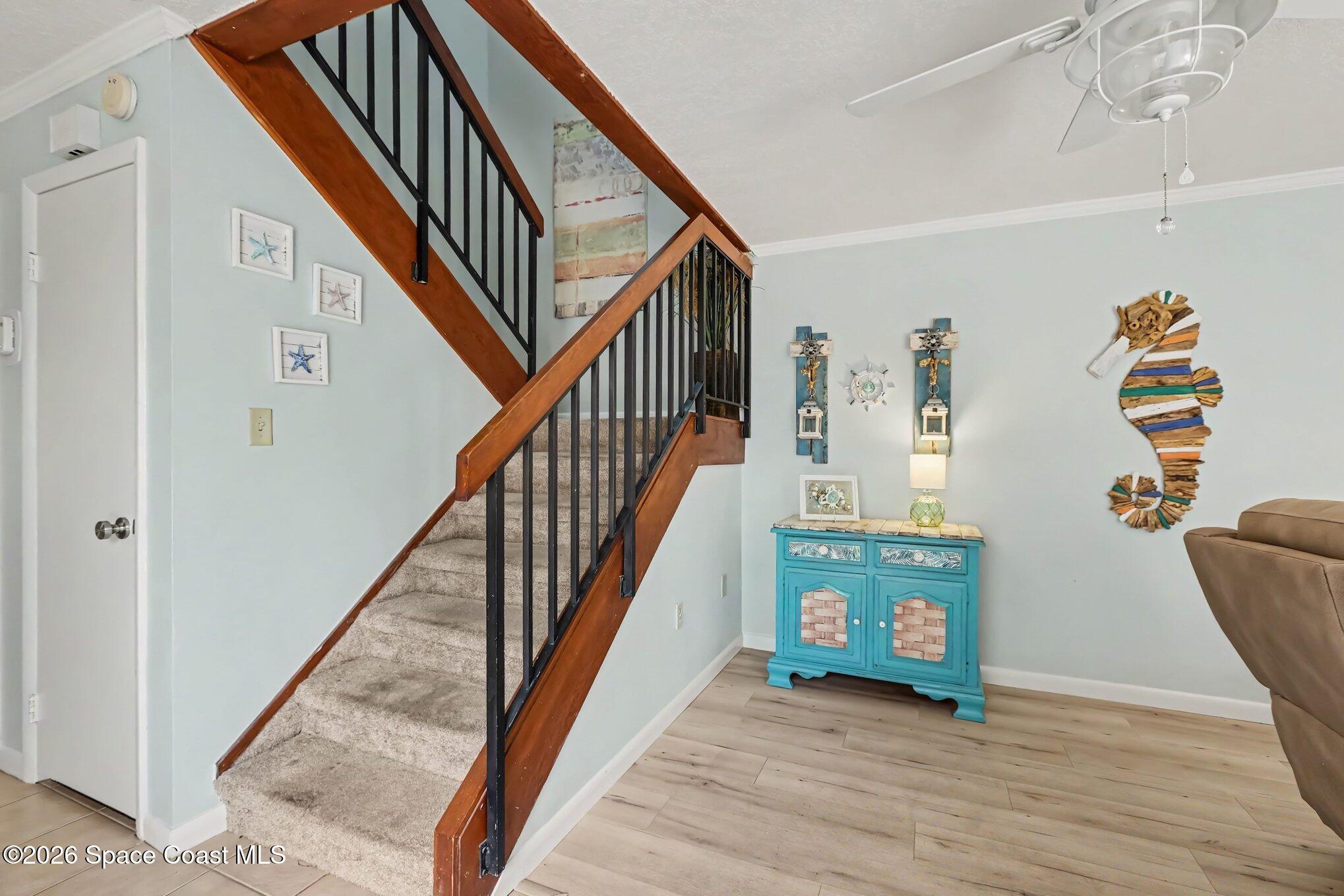 Furnished interior with a carpeted staircase, wood-and-black railing, and turquoise cabinet with coastal decor.