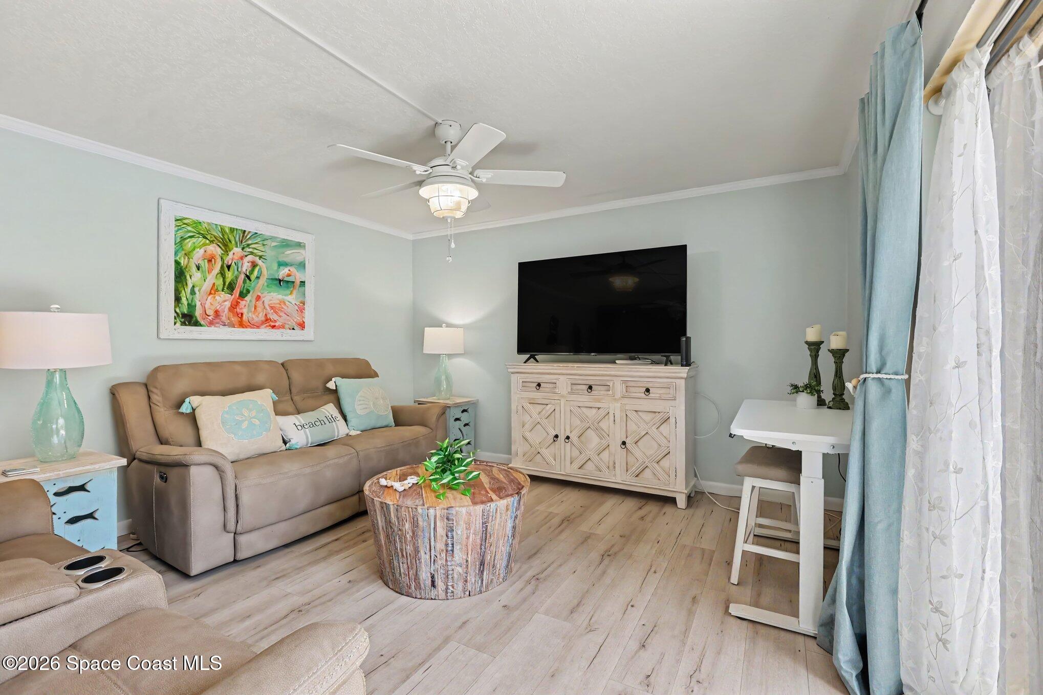 Living room with a tan sofa, flamingo artwork, round wood coffee table, and coastal blue curtains.