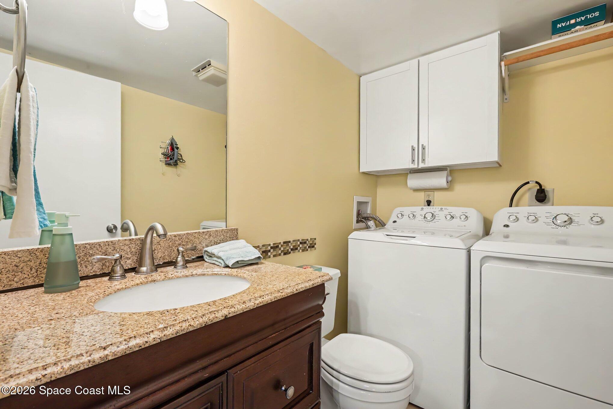 Bathroom with granite vanity and washer and dryer beside the toilet.