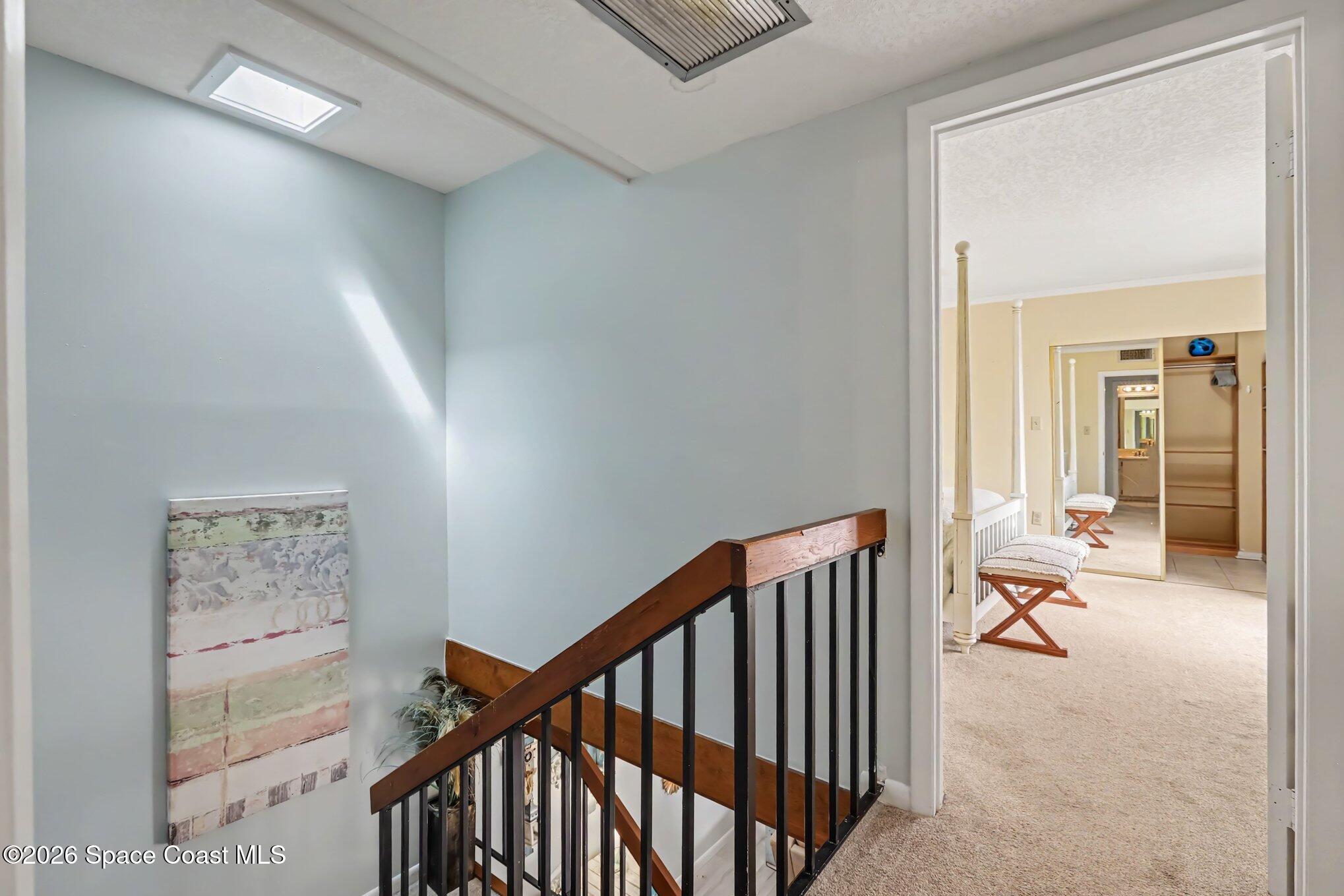 Stair landing with a dark wood railing, skylight, and doorway to a carpeted bedroom.