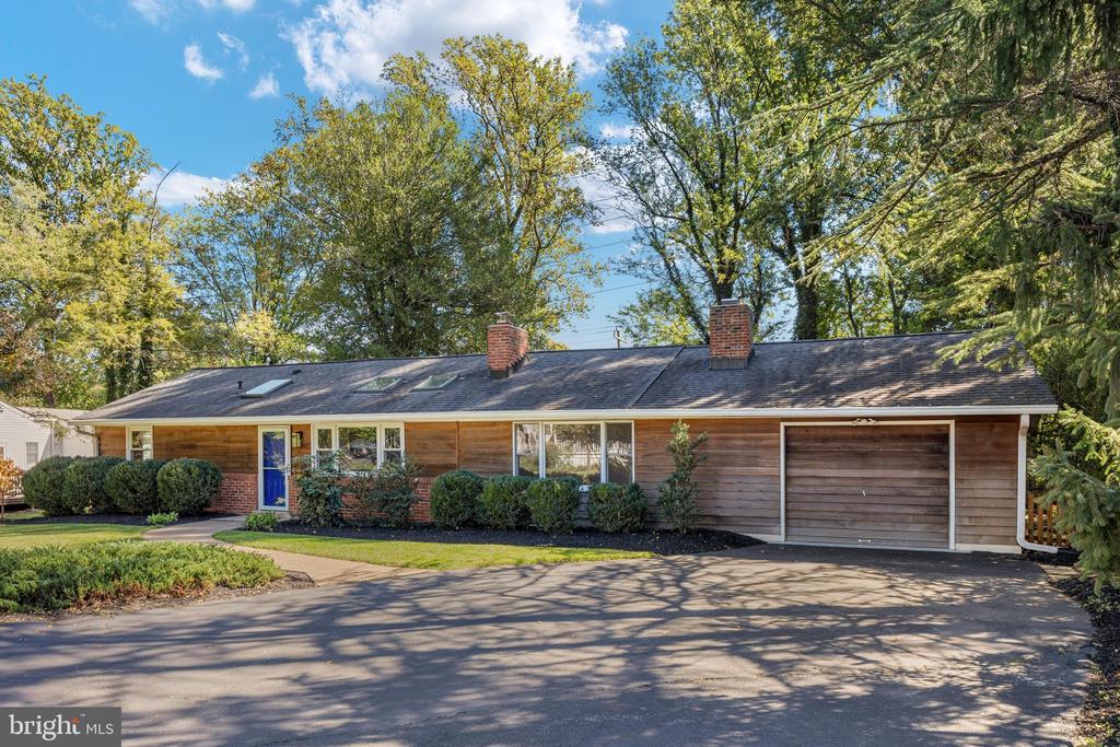 Ranch house with brown wood siding, blue front door, attached garage, and mature trees.