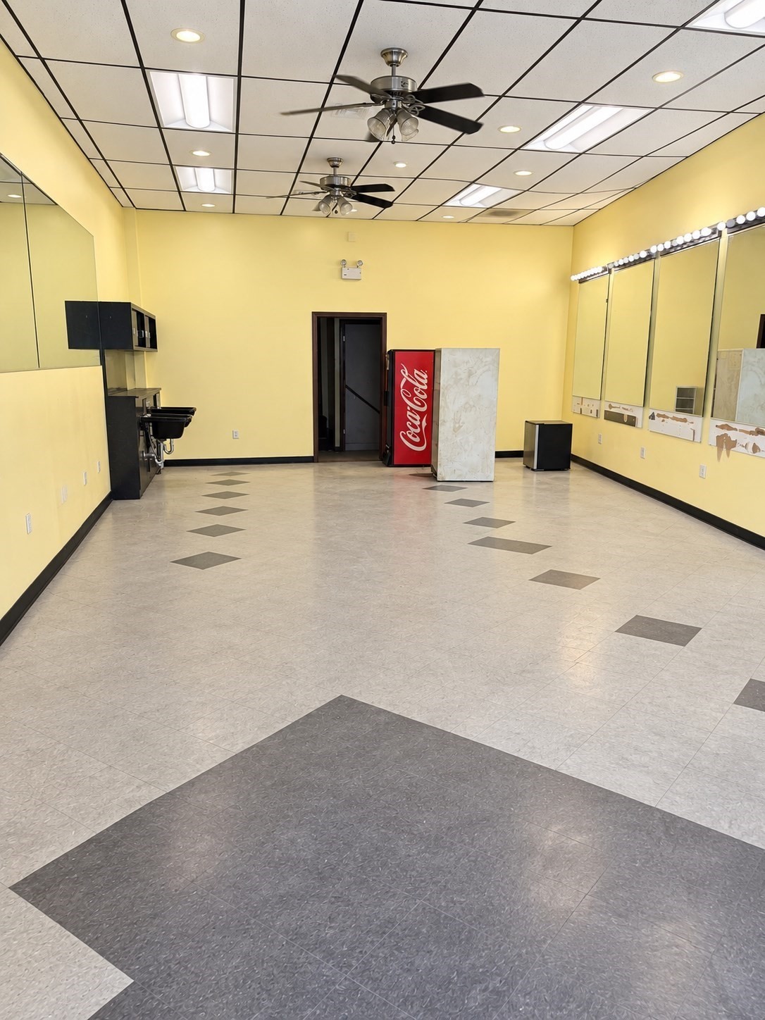 Vacant salon interior with wall mirrors, wash stations, and a Coca-Cola vending machine.